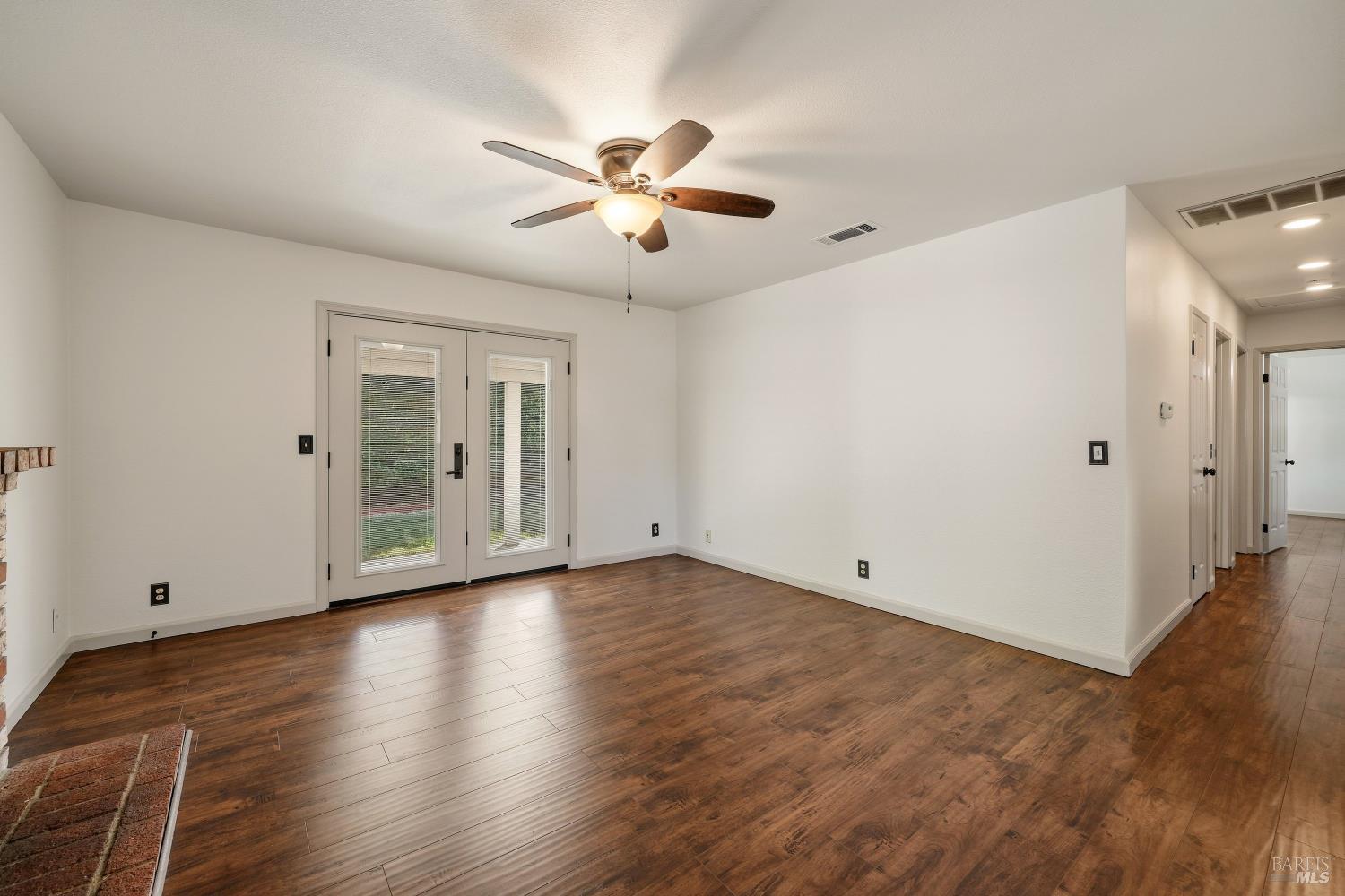 Empty living area with dark wood floors, French doors, and a ceiling fan.
