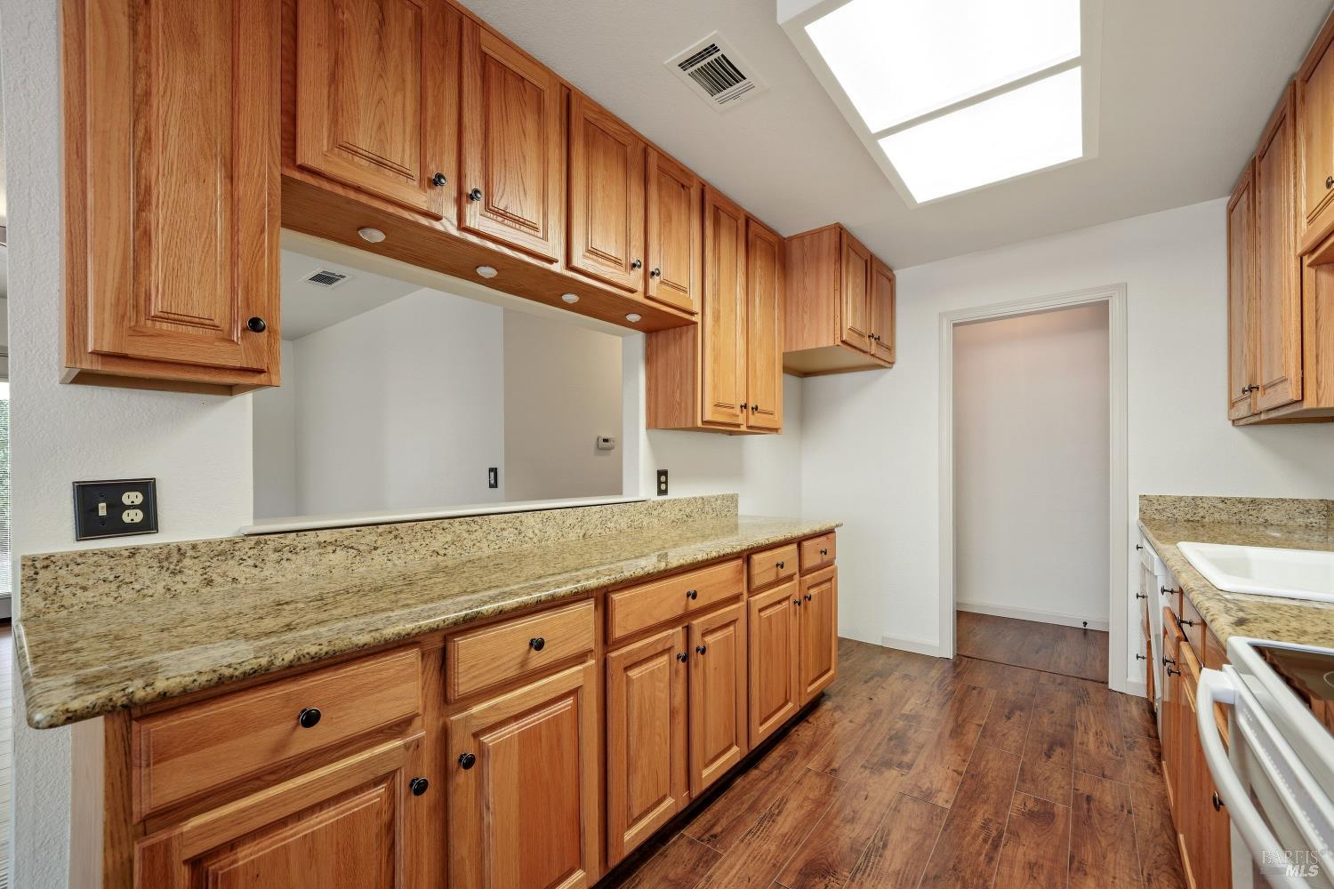 Kitchen with honey-toned wood cabinets, stone counters, and a large skylight.