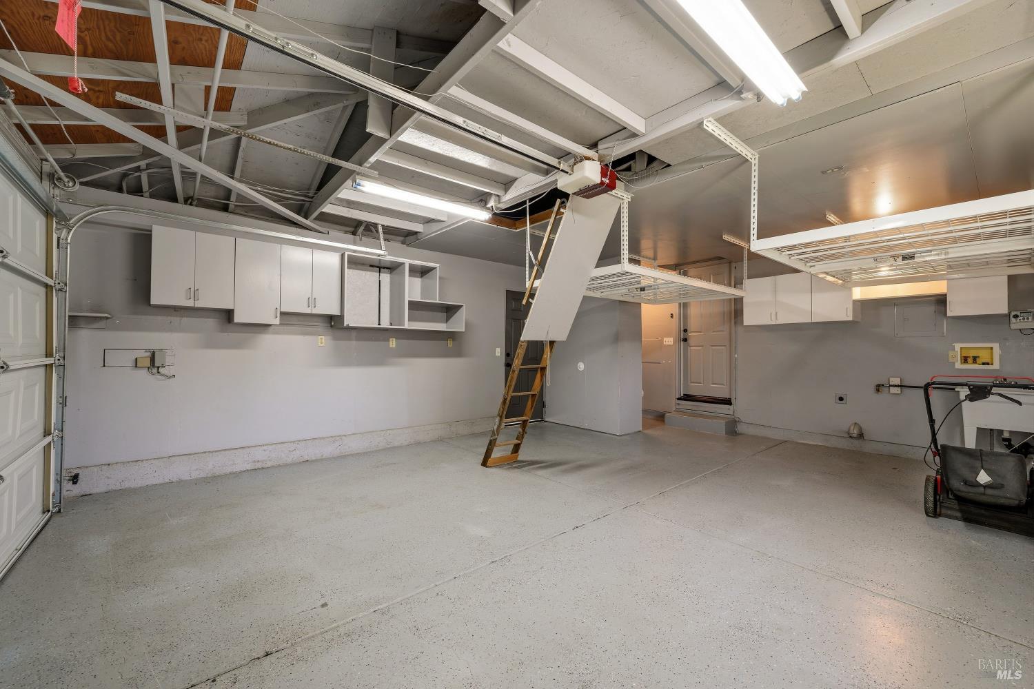 Garage with built-in cabinets, overhead storage racks, and a pull-down attic ladder.