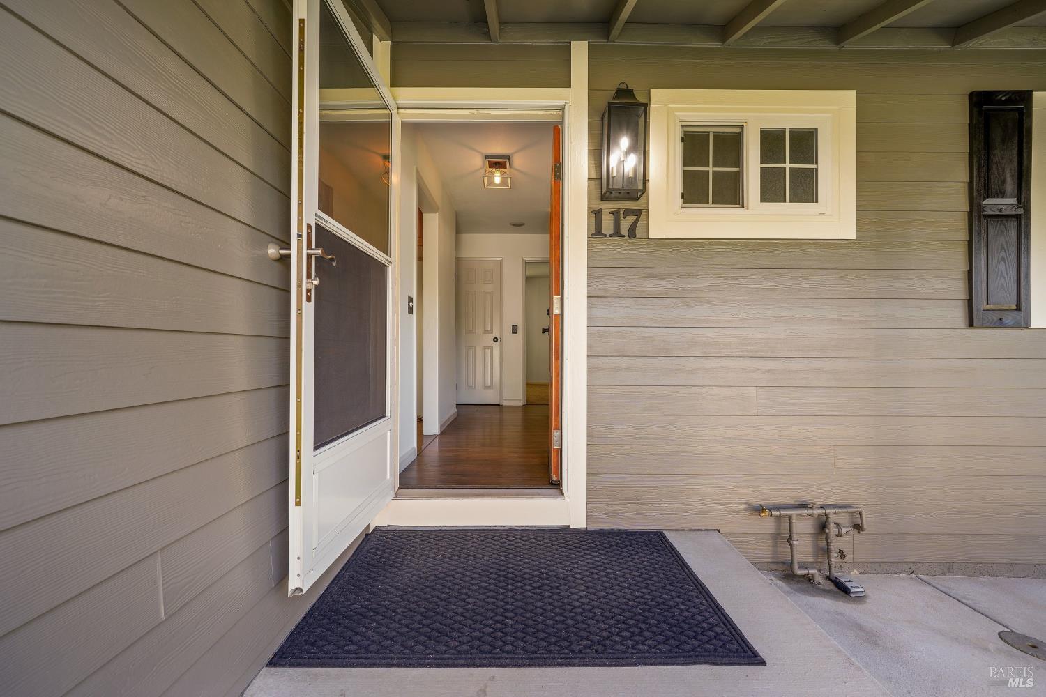 Covered front entrance with open screen door, house number 117, and dark porch mat.