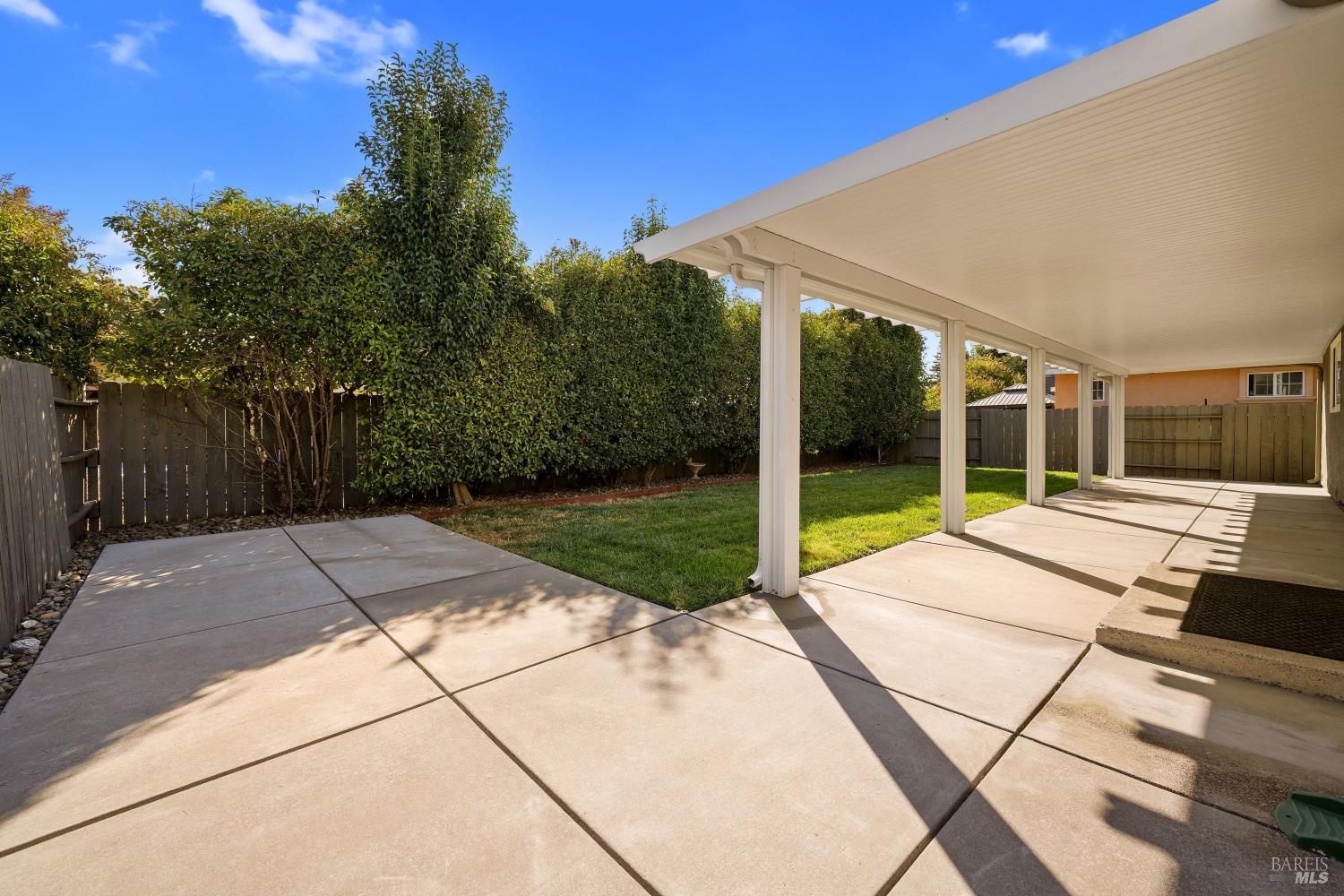 Backyard with a covered patio, small lawn, and tall hedges along the fence.