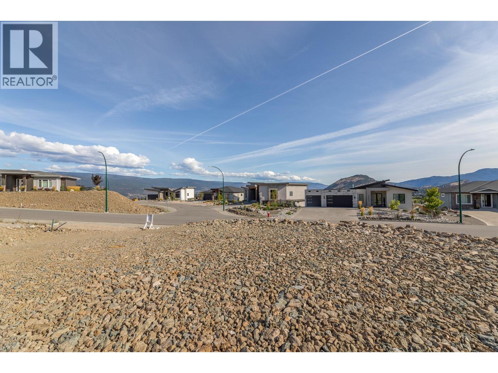 Rocky vacant lot overlooking modern homes and distant mountains.