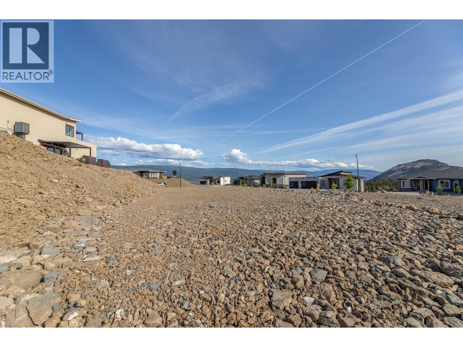 Rocky vacant lot with modern homes and distant mountain views.