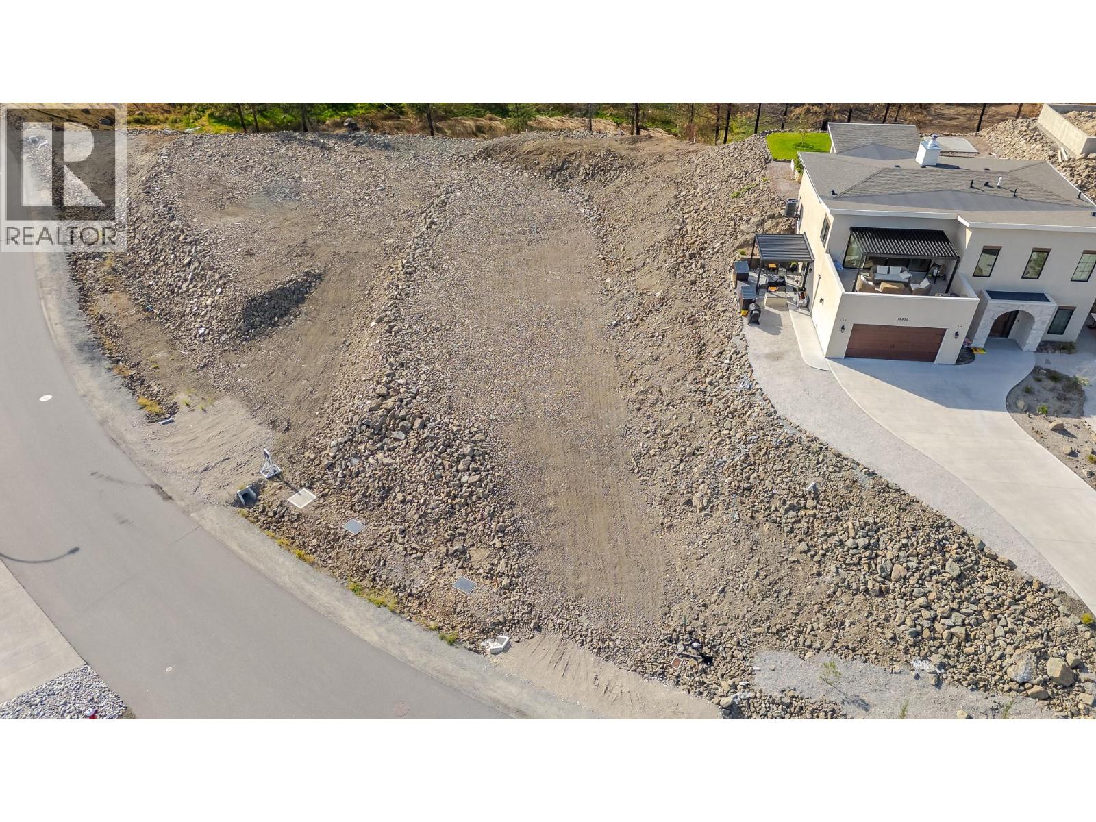 Aerial view of a rocky vacant lot beside a modern white house and paved road.