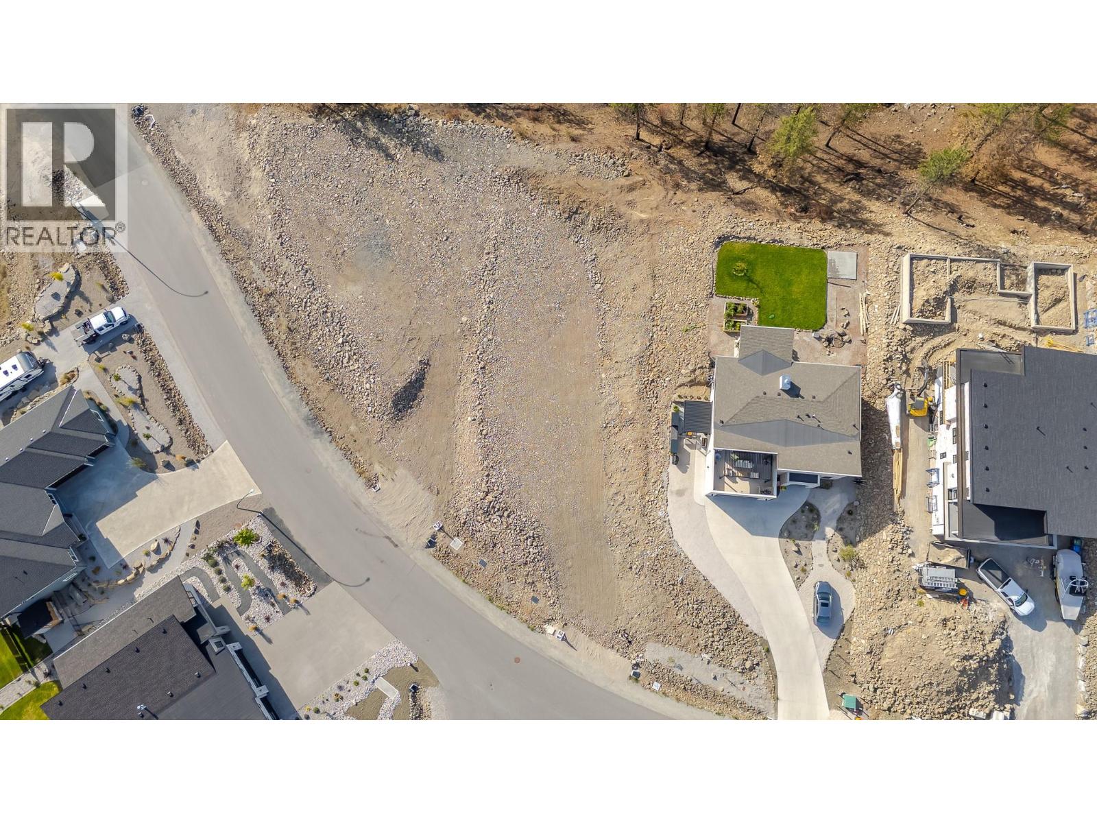 Aerial view of a rocky vacant lot beside a curved road, surrounded by homes.