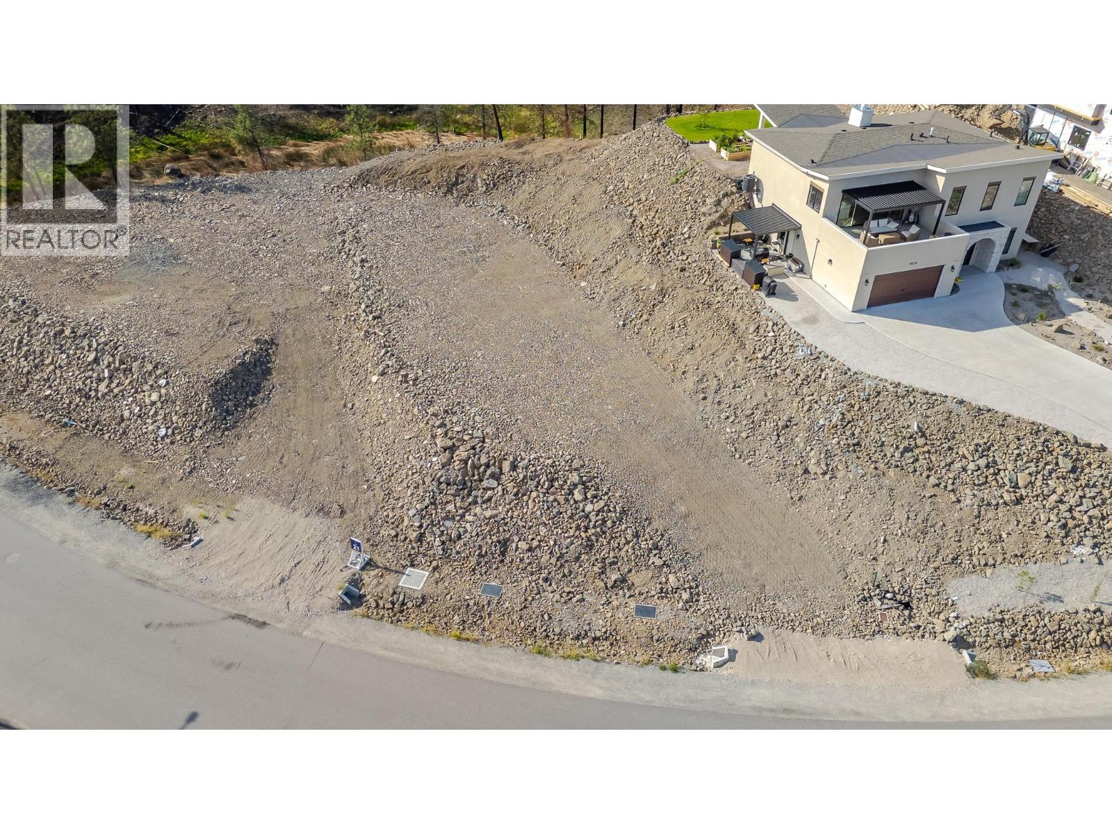 Aerial view of a rocky vacant lot beside a modern house and paved road.