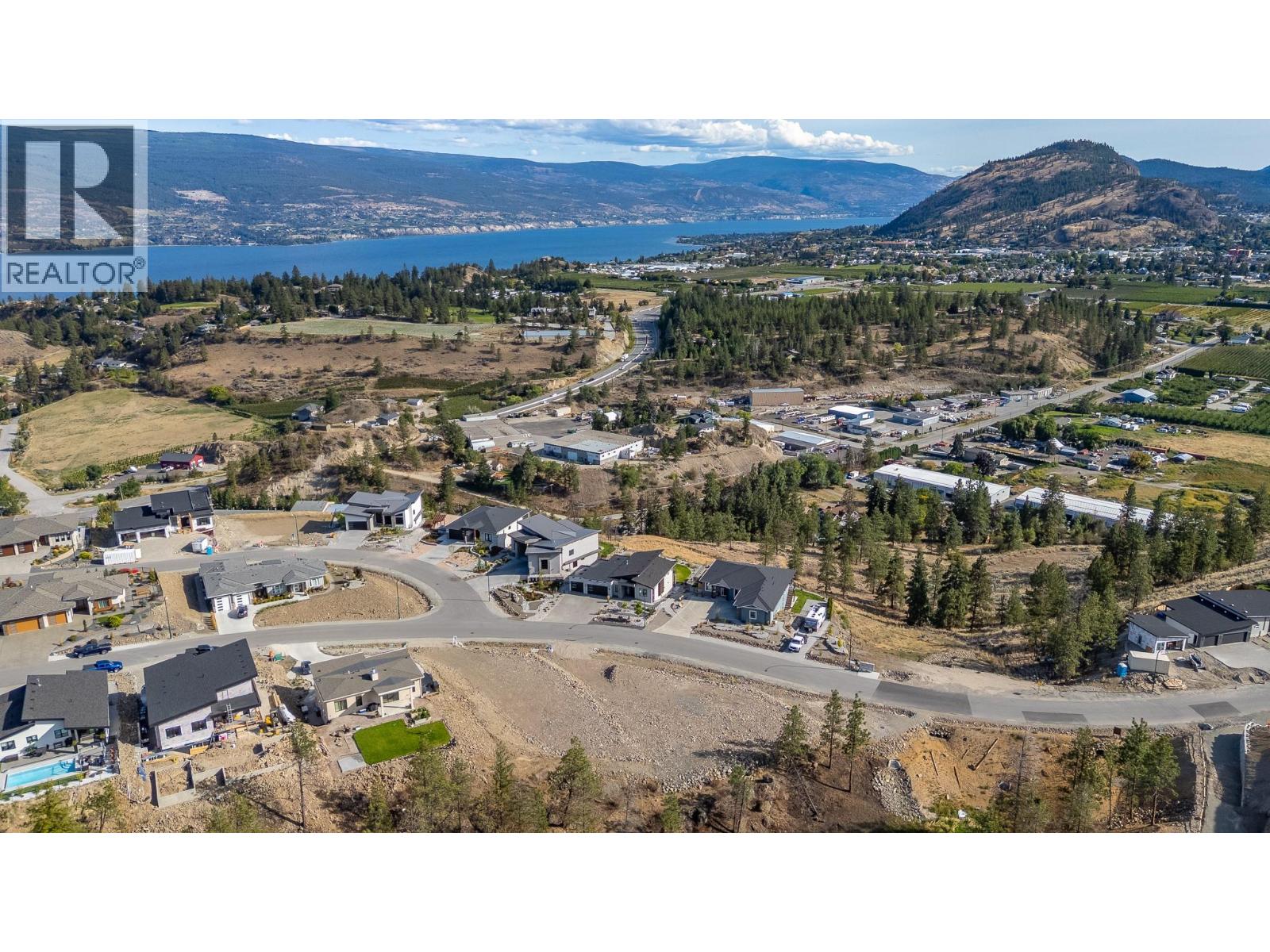 Aerial view of a residential subdivision, with vacant lots, a lake, and hills in the distance.