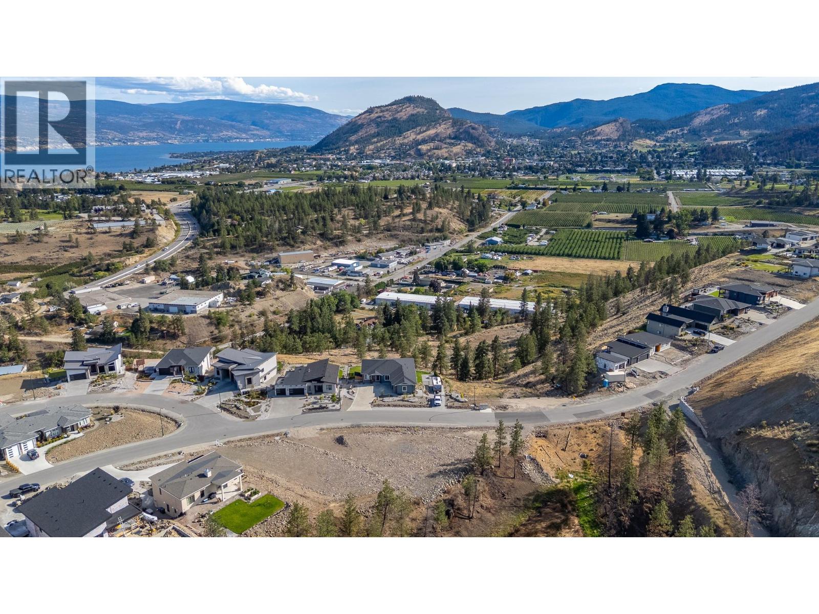 Aerial view of a vacant residential lot with orchards, a lake, and mountains in the distance.