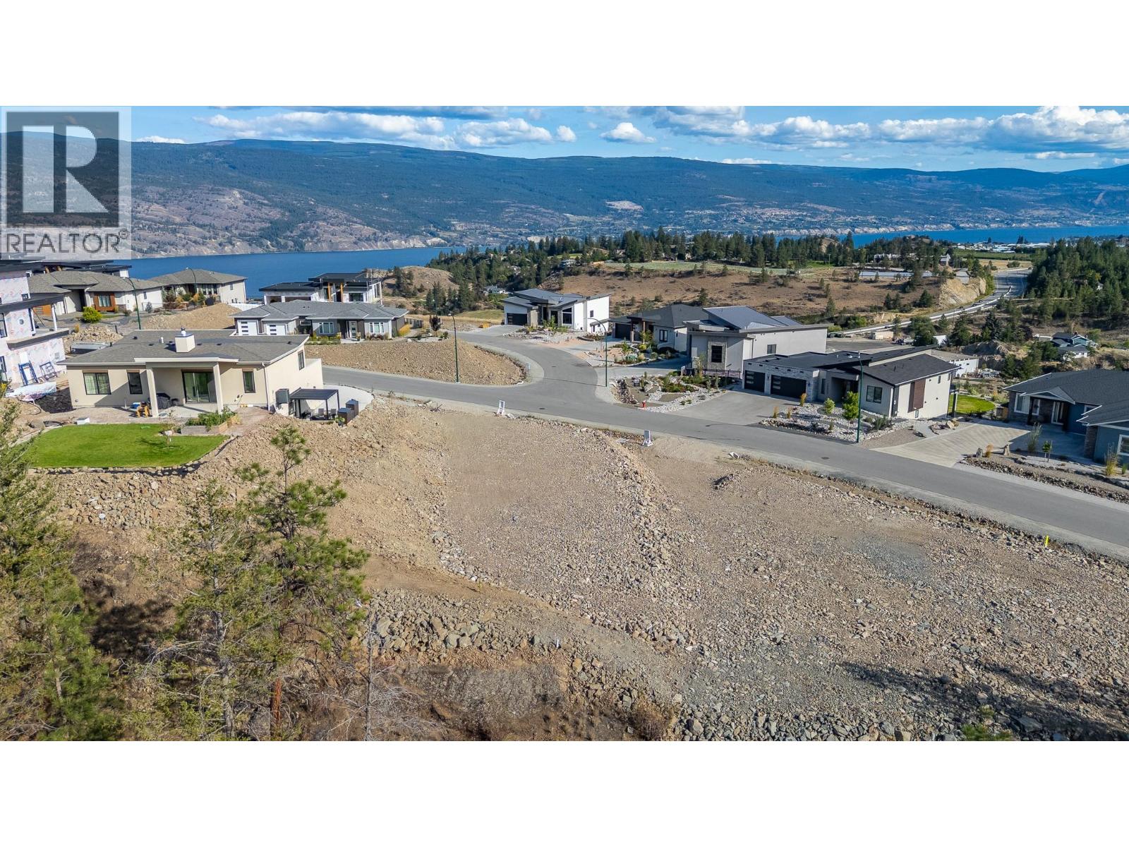 Vacant rocky lot in a hillside subdivision overlooking a lake and distant mountains.