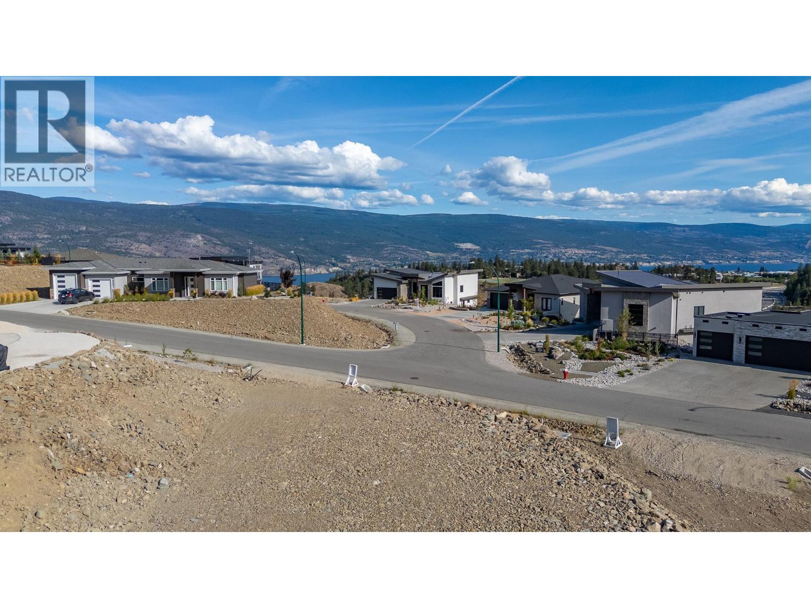 Vacant rocky lot in a hillside neighborhood, with a lake and mountains in the distance.
