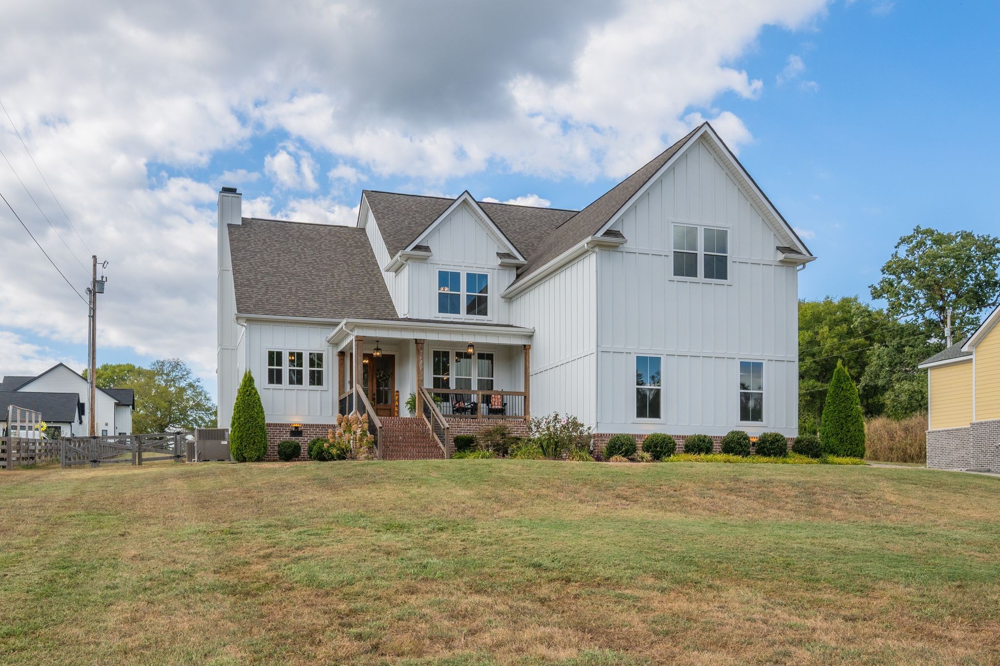 White two-story home with multiple gables, brick foundation, and a covered front porch.