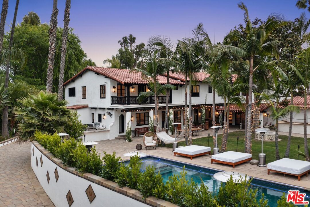 Mediterranean-style home with a courtyard pool, tiled roofs, and palm trees at dusk.
