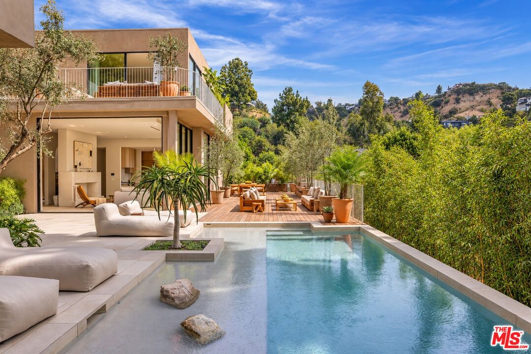 Modern home with a long pool, furnished terrace, and hillside views.
