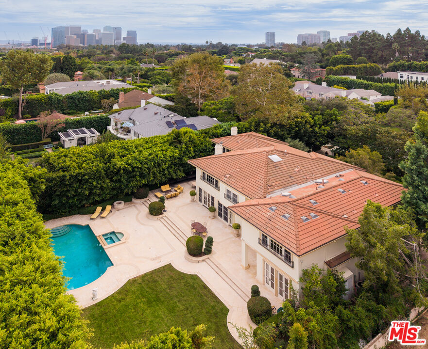 Beverly Hills home with terracotta tile roofs, a backyard pool, and a distant city skyline.