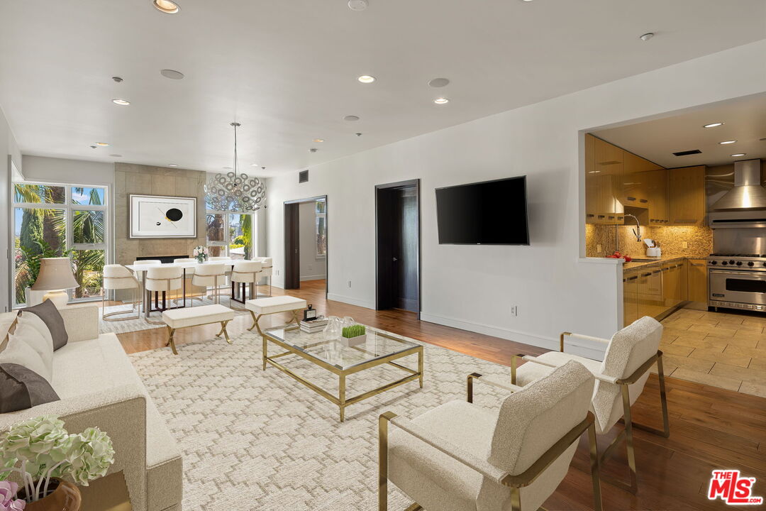Furnished condo living room with a glass coffee table, dining area, and open wood-cabinet kitchen.