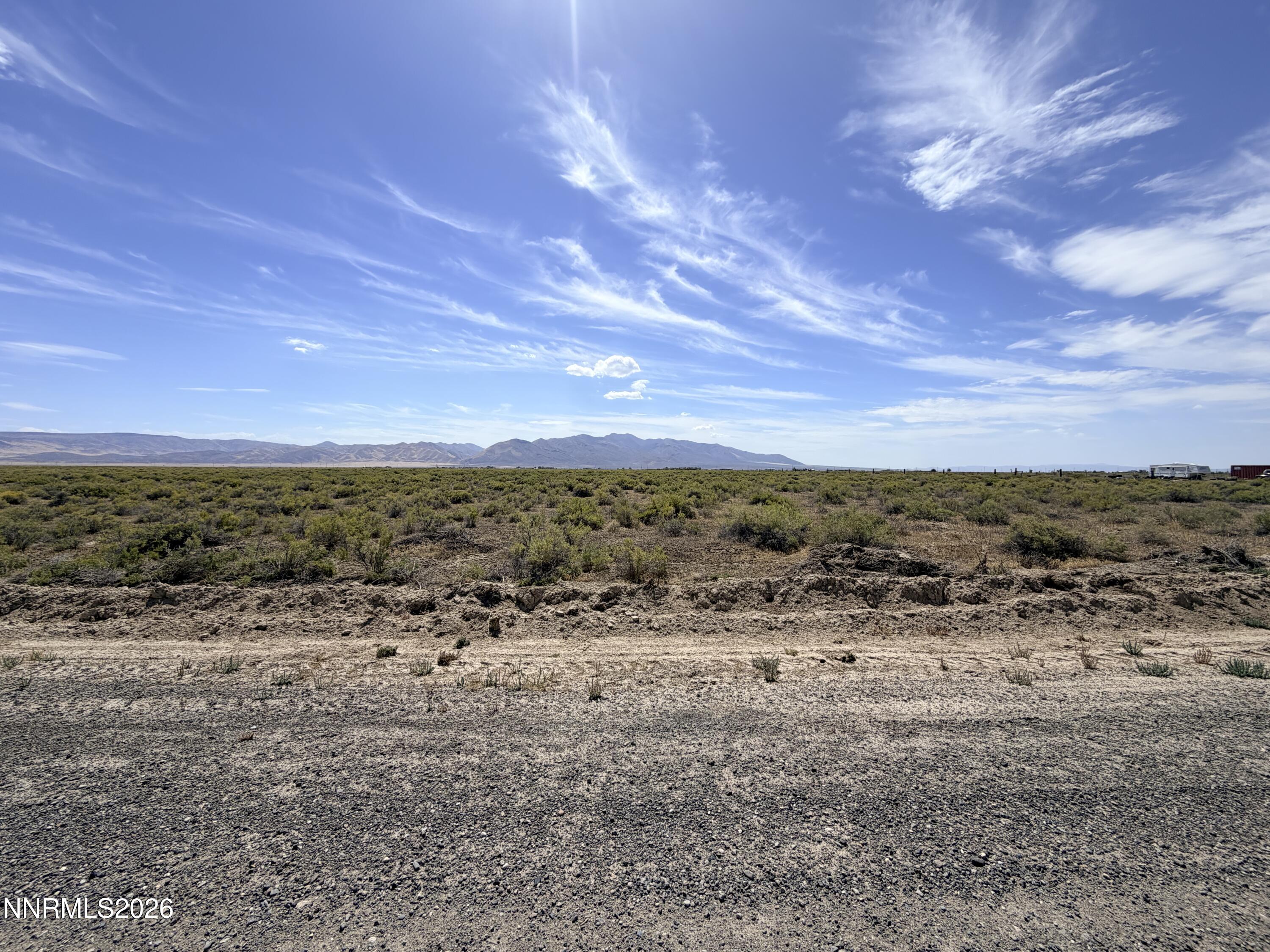 Open desert land with sparse scrub and rocky ground, backed by distant mountains beneath a cloud-streaked sky.