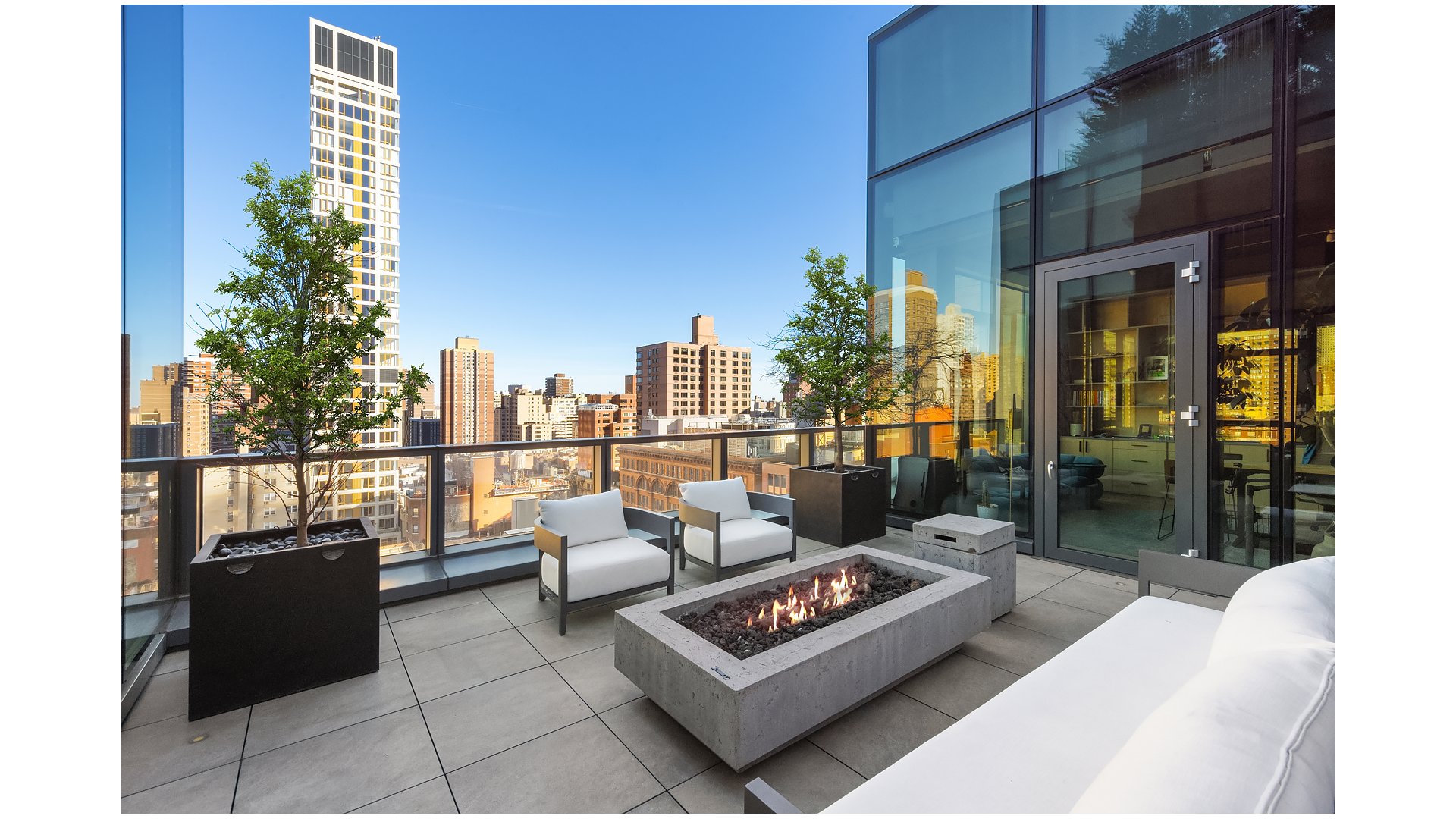 Rooftop terrace with a rectangular fire pit, white lounge chairs, and city skyline views.