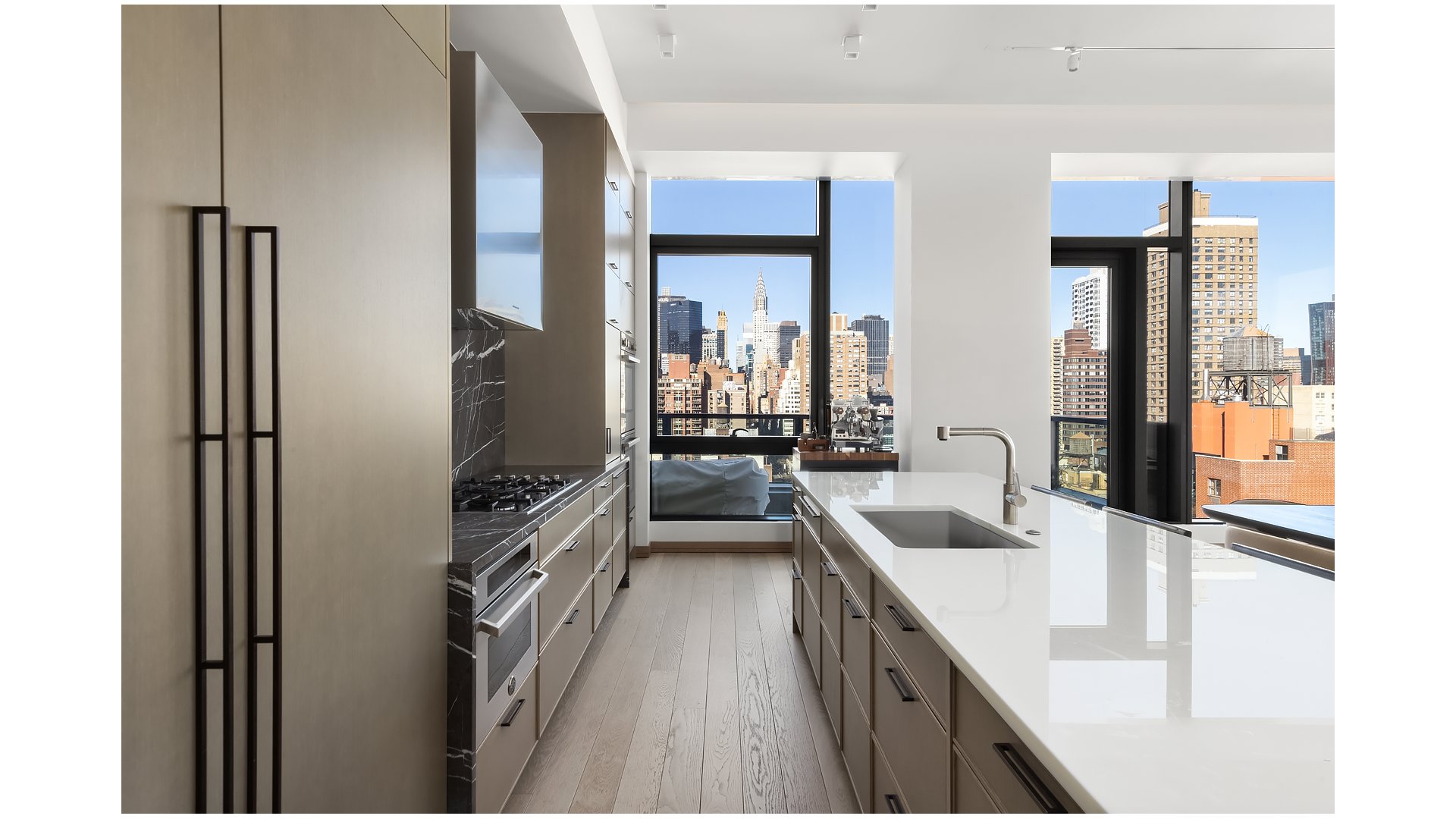 Modern kitchen with a long white island and Manhattan skyline views through floor-to-ceiling windows.