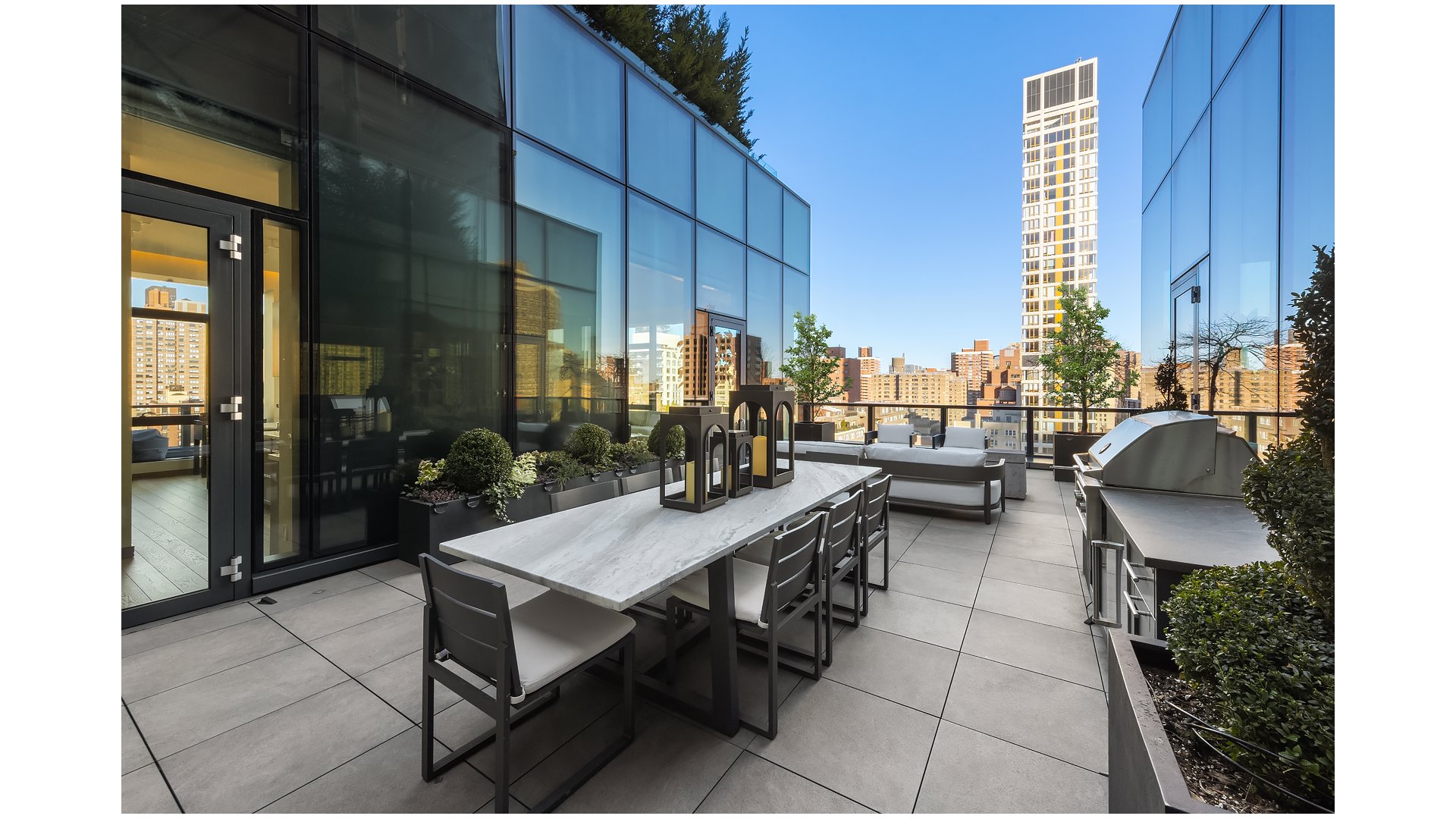 Rooftop terrace with a long dining table, lounge seating, planters, and city skyline views.