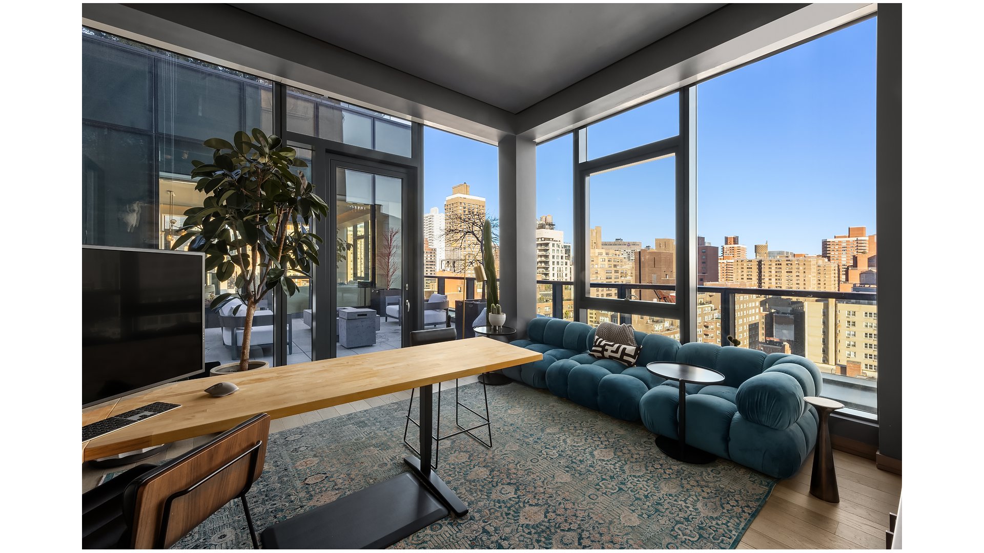 High-rise living room with a teal sectional and expansive city views through floor-to-ceiling windows.