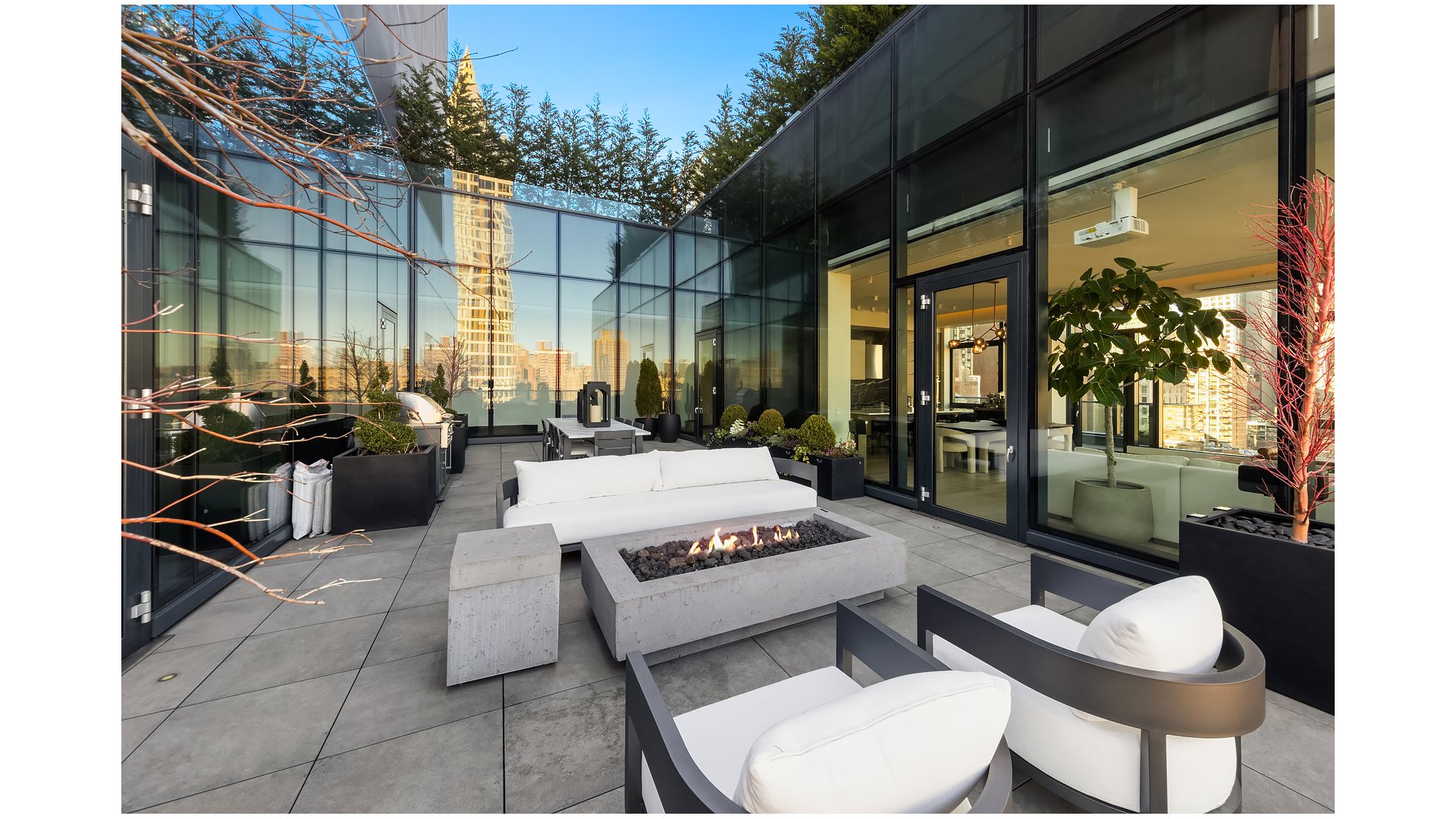 Furnished rooftop terrace with glass walls, outdoor seating, and a long gas fire pit.