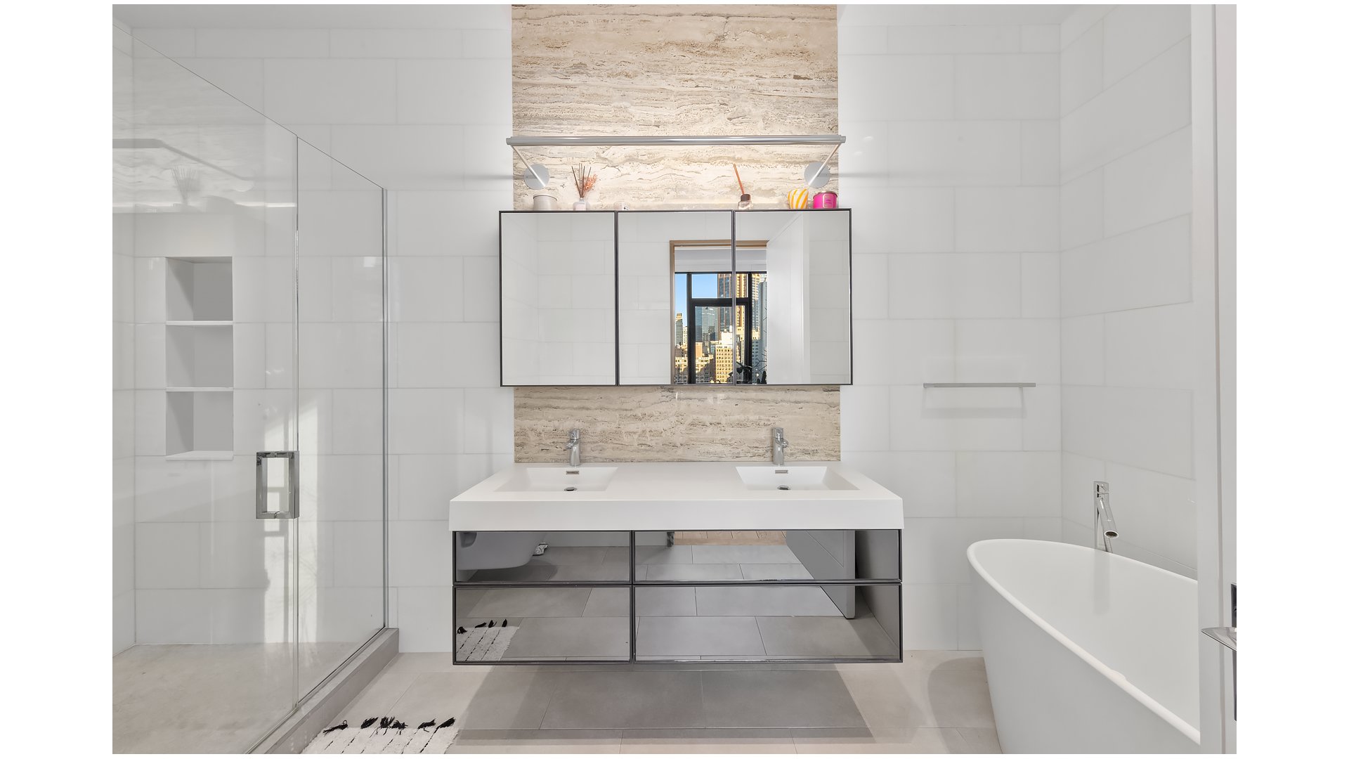Modern bathroom with a double vanity, glass shower, soaking tub, and city buildings reflected in the mirror.