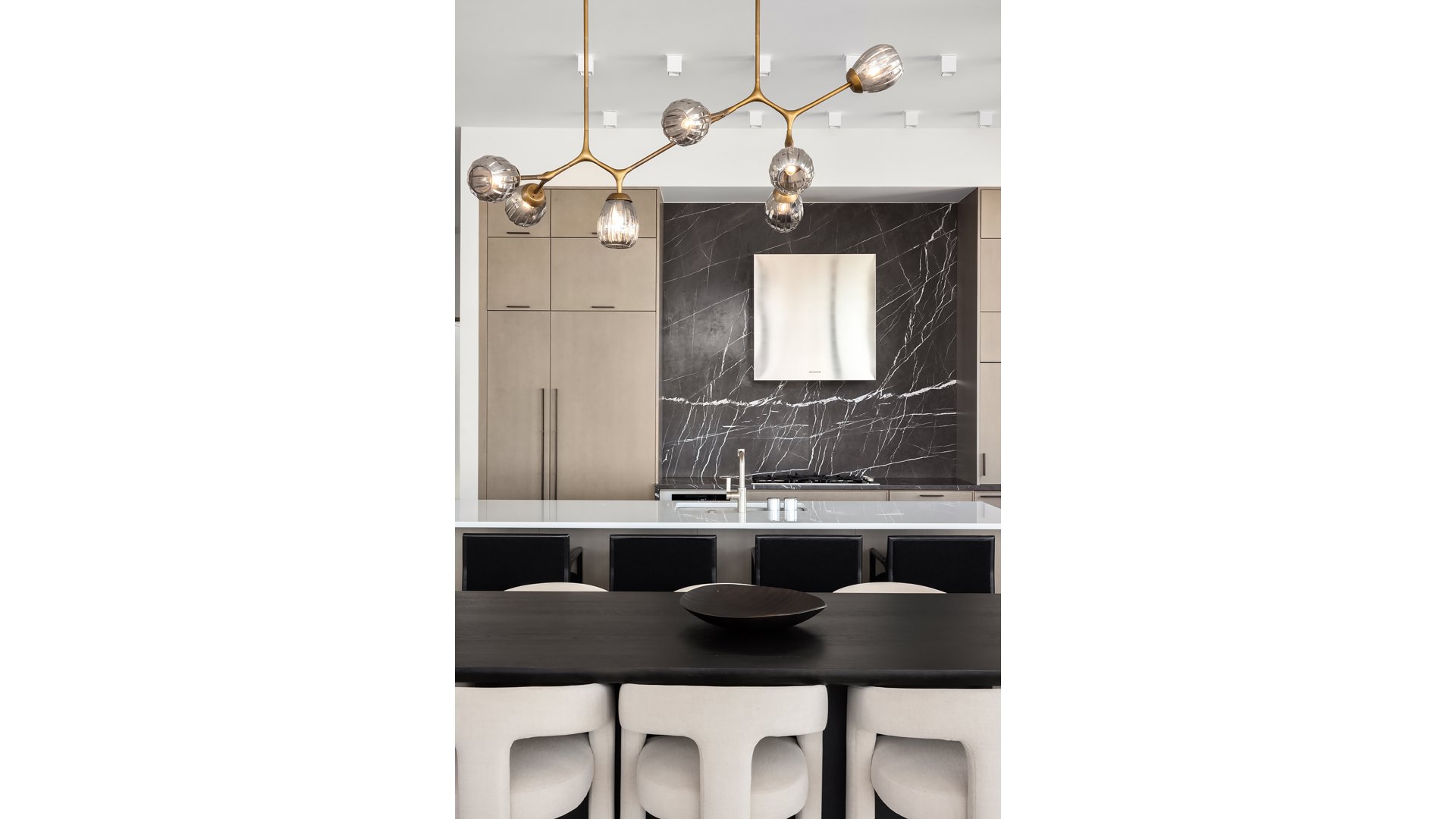 Modern kitchen with a black marble backsplash, white island, and sculptural brass pendant lights.