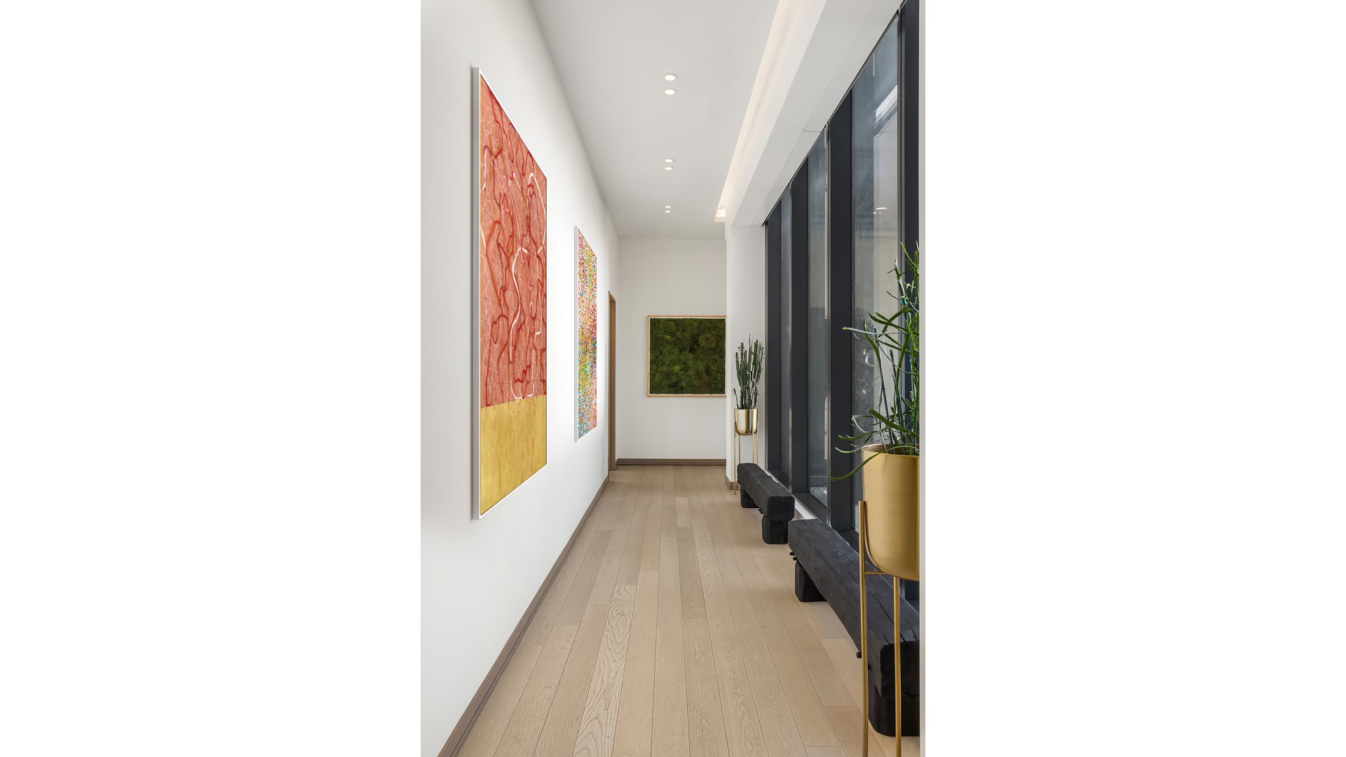 Modern apartment hallway with pale wood floors, colorful artwork, and tall windows.