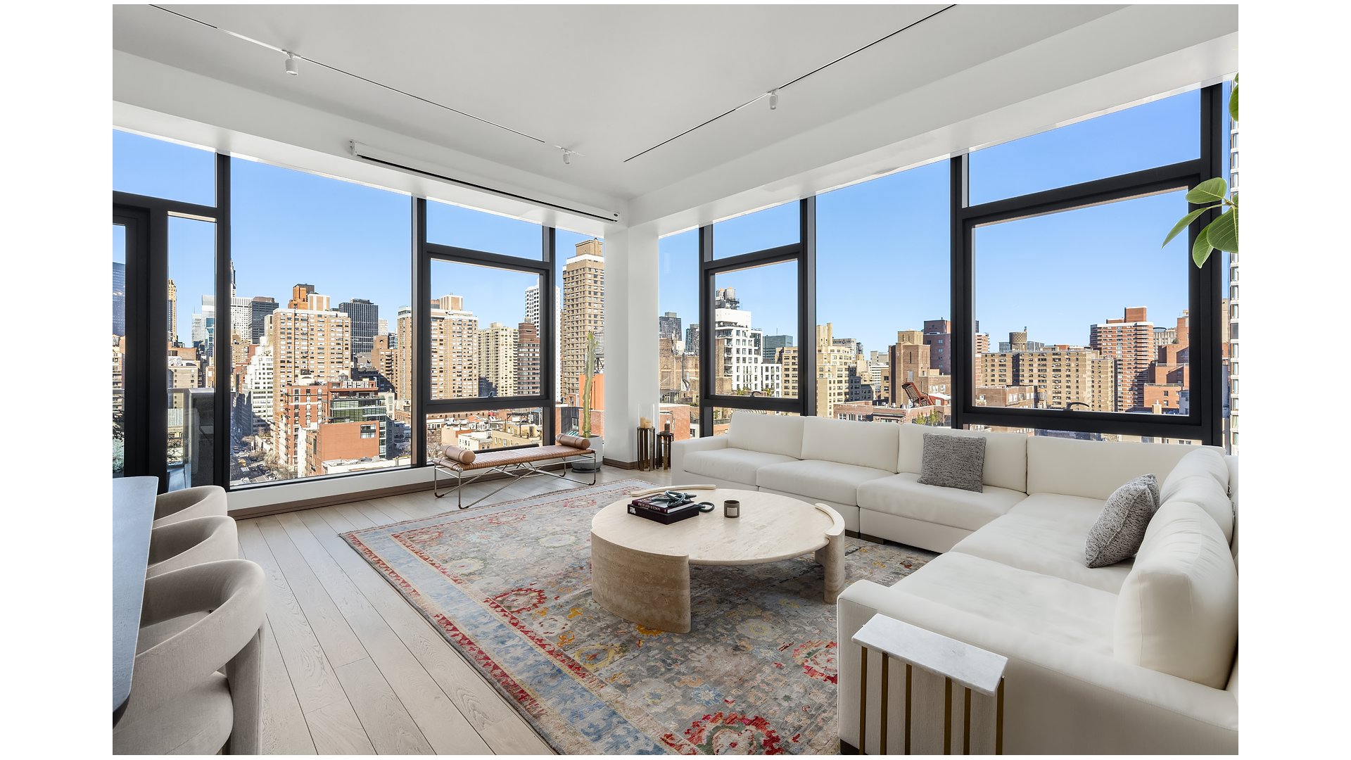 Staged living room with floor-to-ceiling windows, a white sectional, and city skyline views.