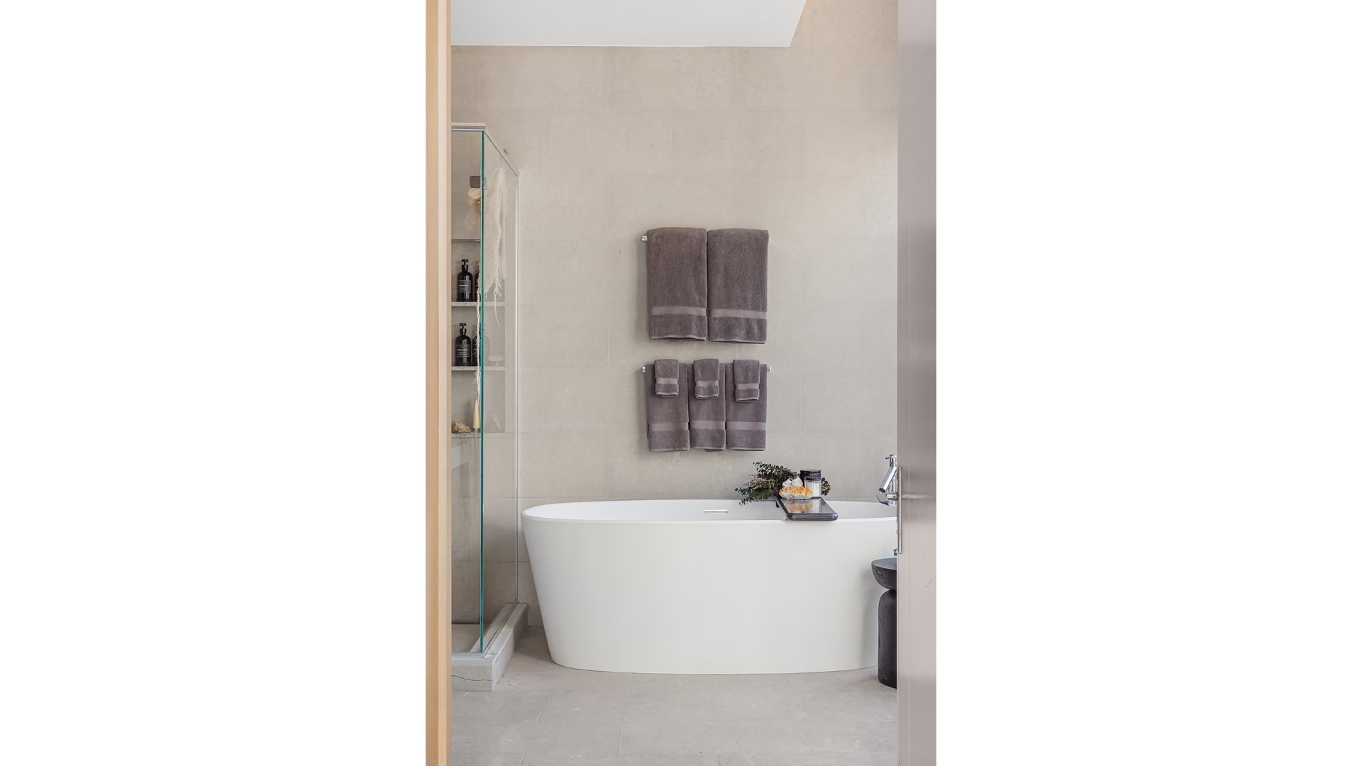 Bathroom with a freestanding white tub, glass shower, and neatly arranged gray towels.