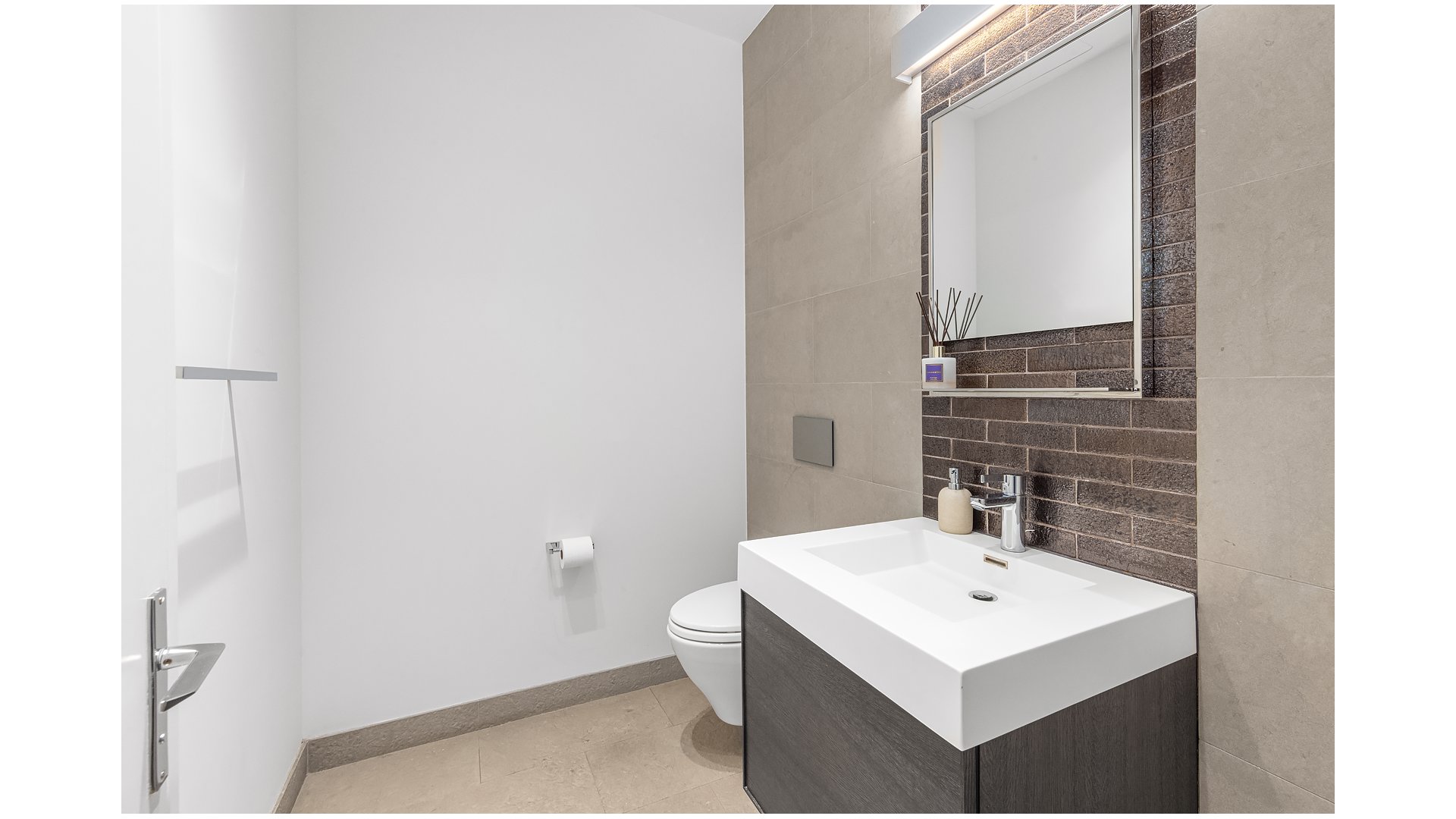 Modern bathroom with a white sink, dark wood vanity, and dark tiled wall.