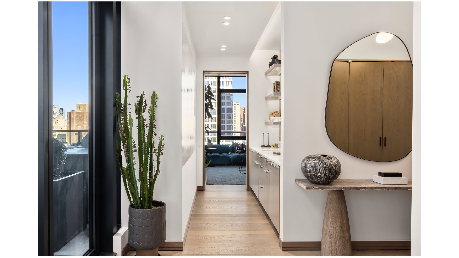 Bright apartment entry hall with pale wood floors, built-in cabinetry, and a city view through tall windows.