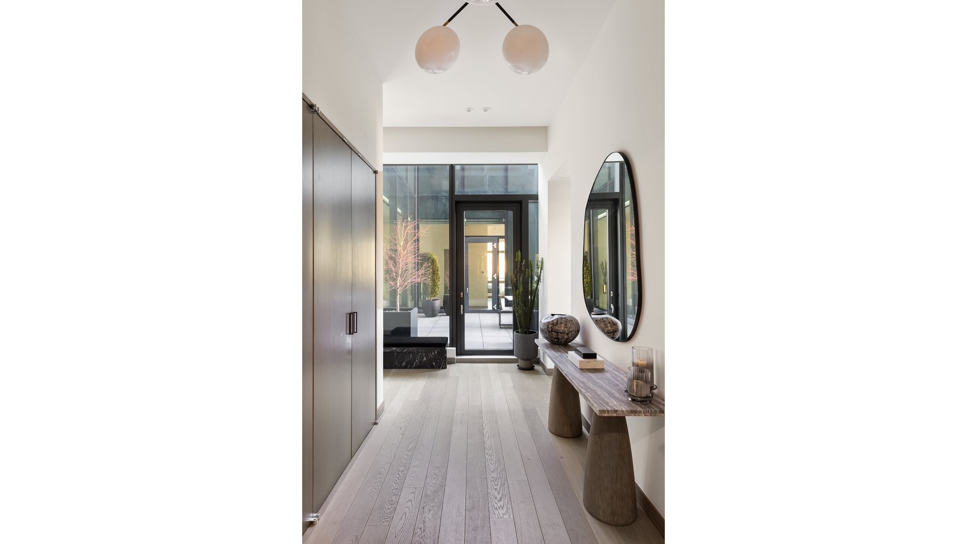 Entry hall with pale wood floors, dark cabinetry, a stone console table, and glass doors to a planted patio.