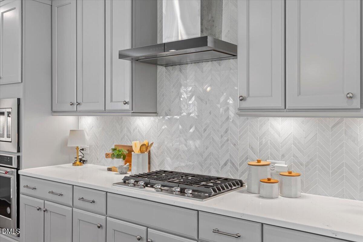 Kitchen with gray shaker cabinets, a wide gas cooktop, and a white herringbone tile backsplash.