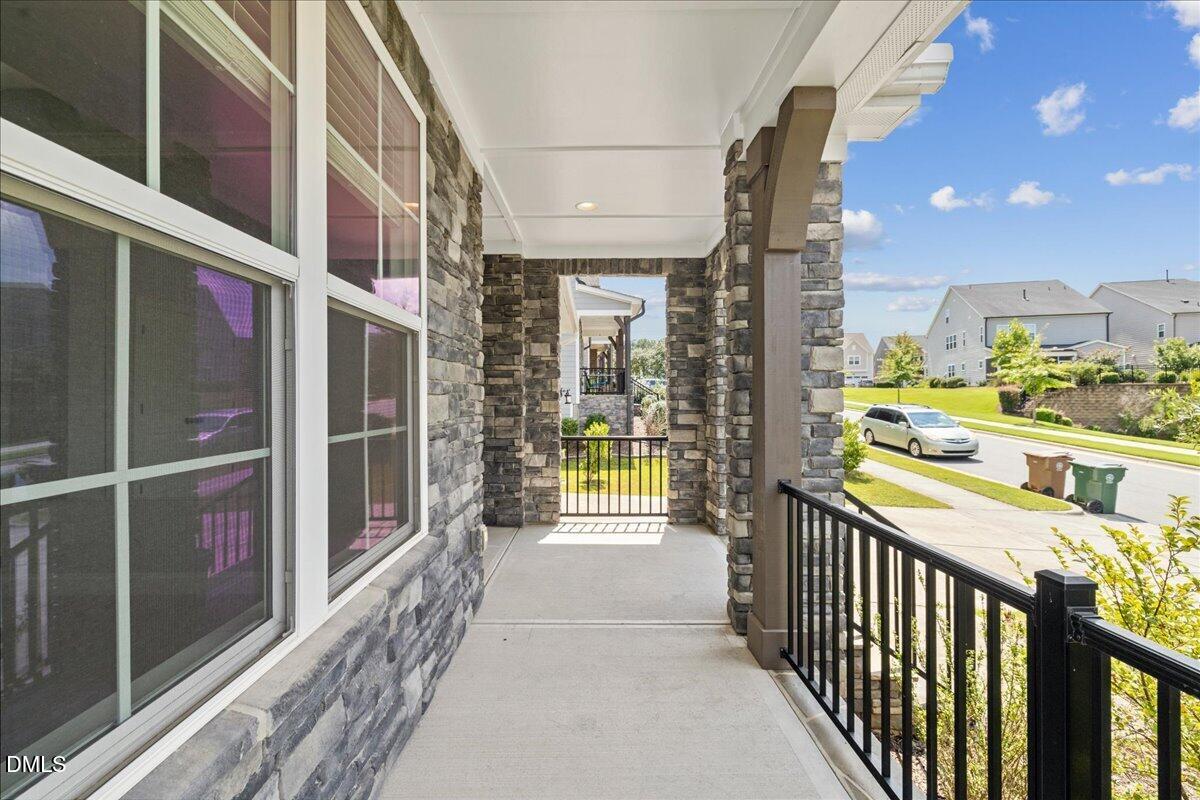 Covered stone-front porch with large windows and black railings overlooking a sunny residential street.