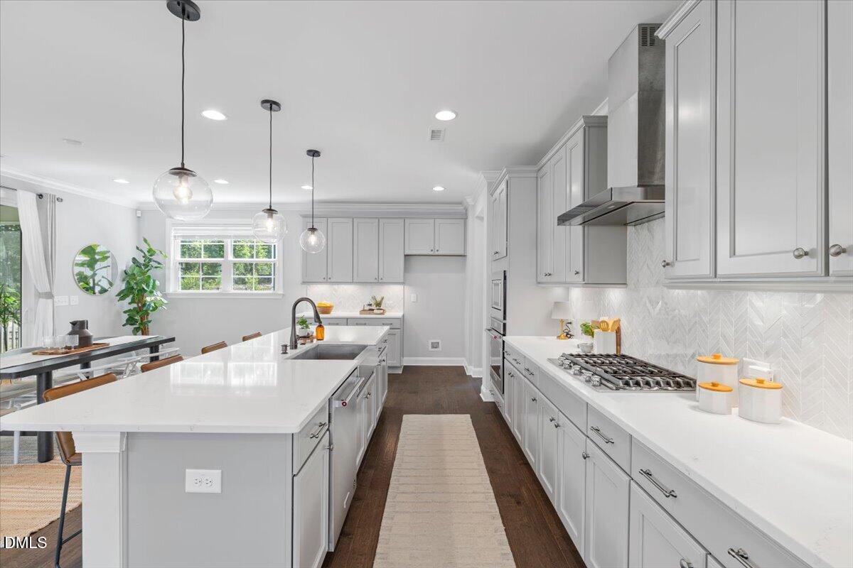 Bright kitchen with white cabinets, a large island, and a gas cooktop beneath a stainless steel hood.