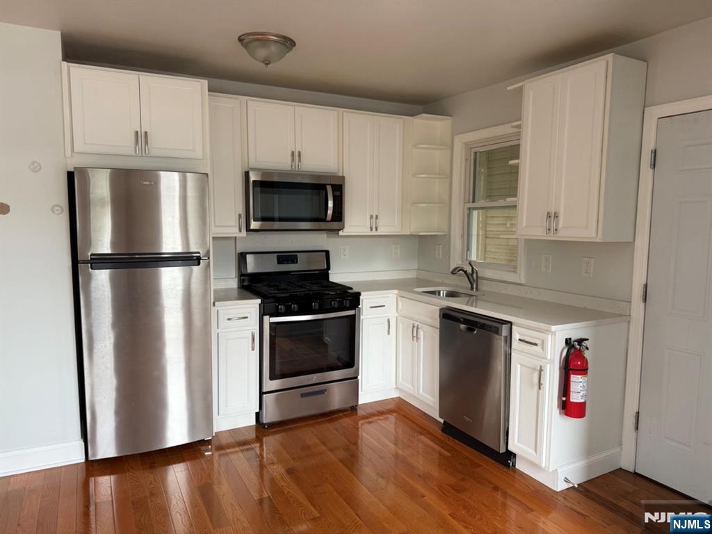 Kitchen with white cabinetry, stainless steel appliances, and glossy hardwood floors.