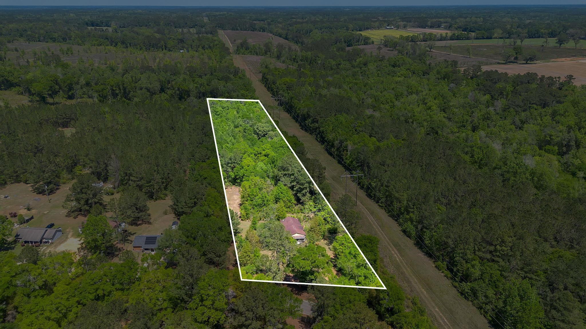Aerial view of a wooded property outlined in white, with a small house near the front.