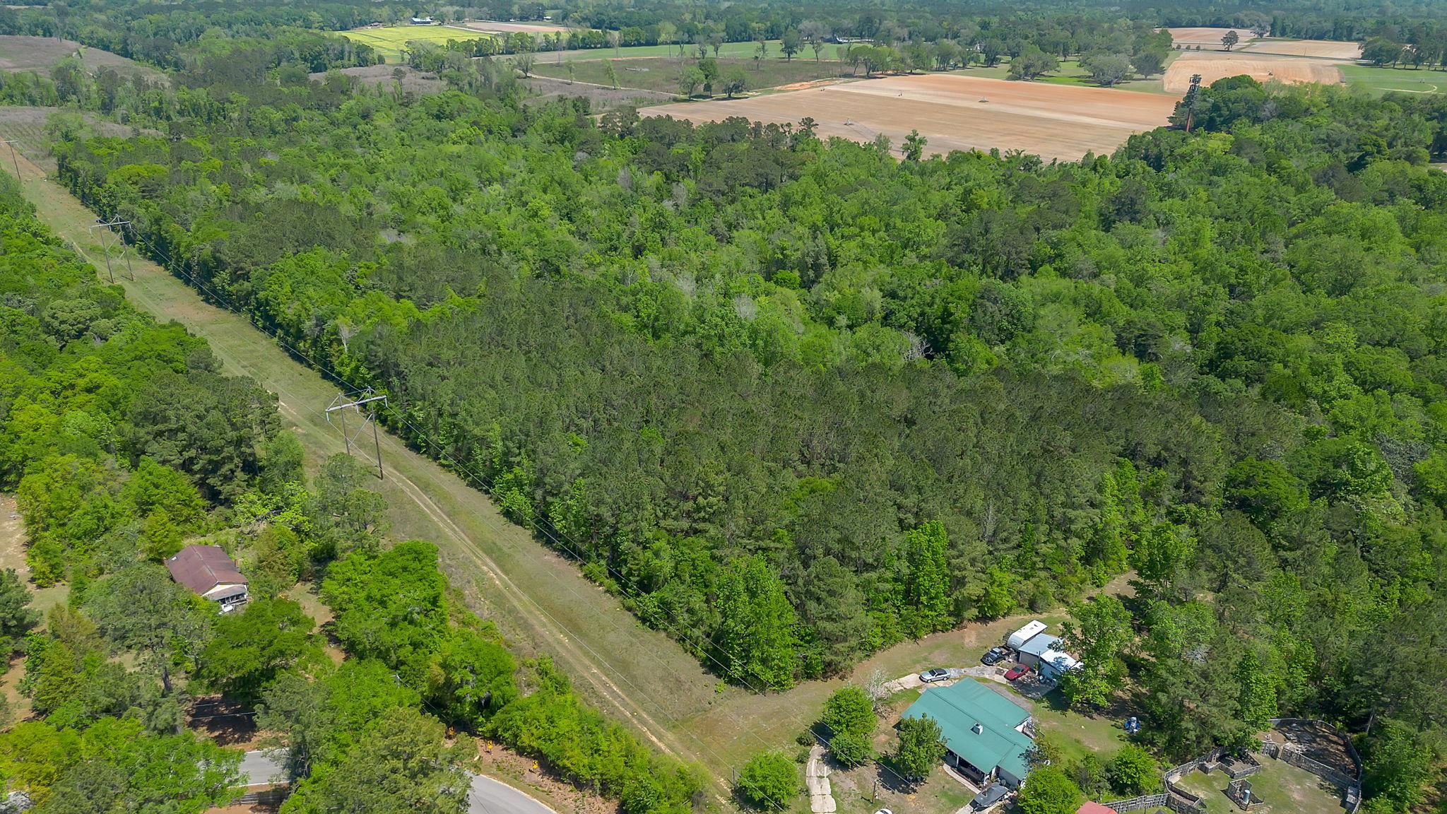 Aerial view of wooded rural land with a power-line easement, neighboring fields, and scattered buildings.