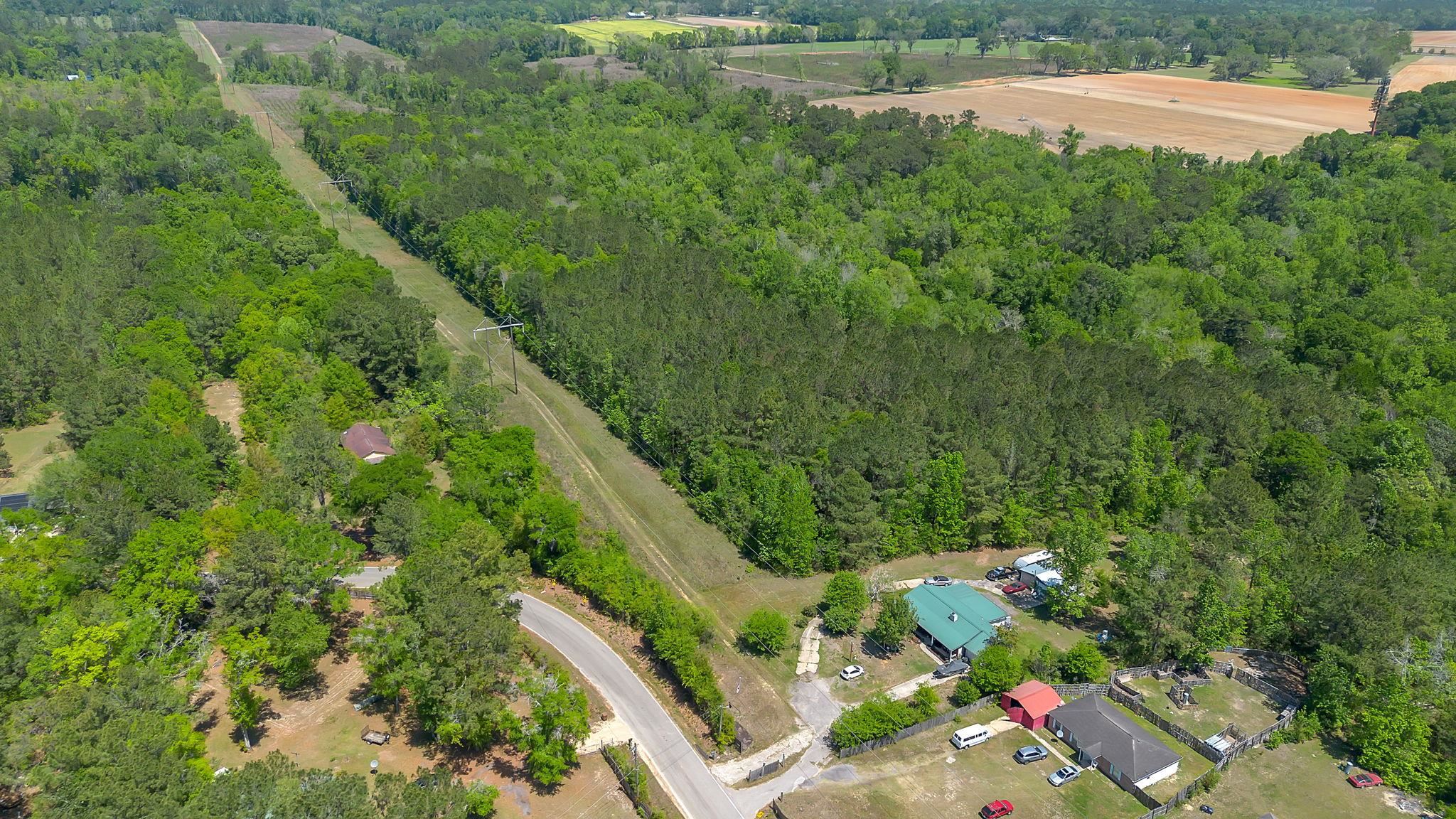 Aerial view of wooded acreage crossed by a utility easement, with nearby homes and farmland.