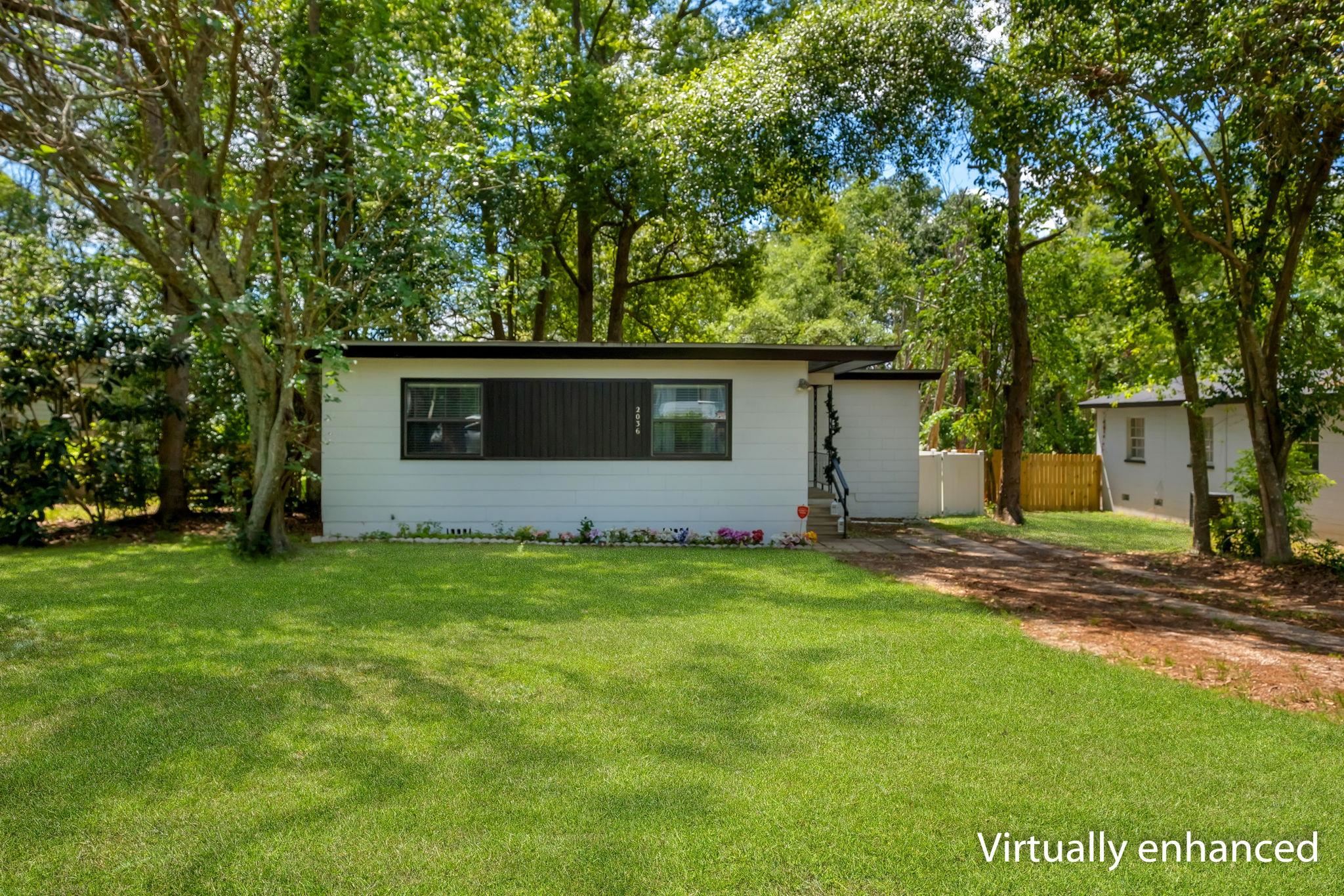 Single-story white home with a dark horizontal window feature, surrounded by mature trees and a broad green lawn.