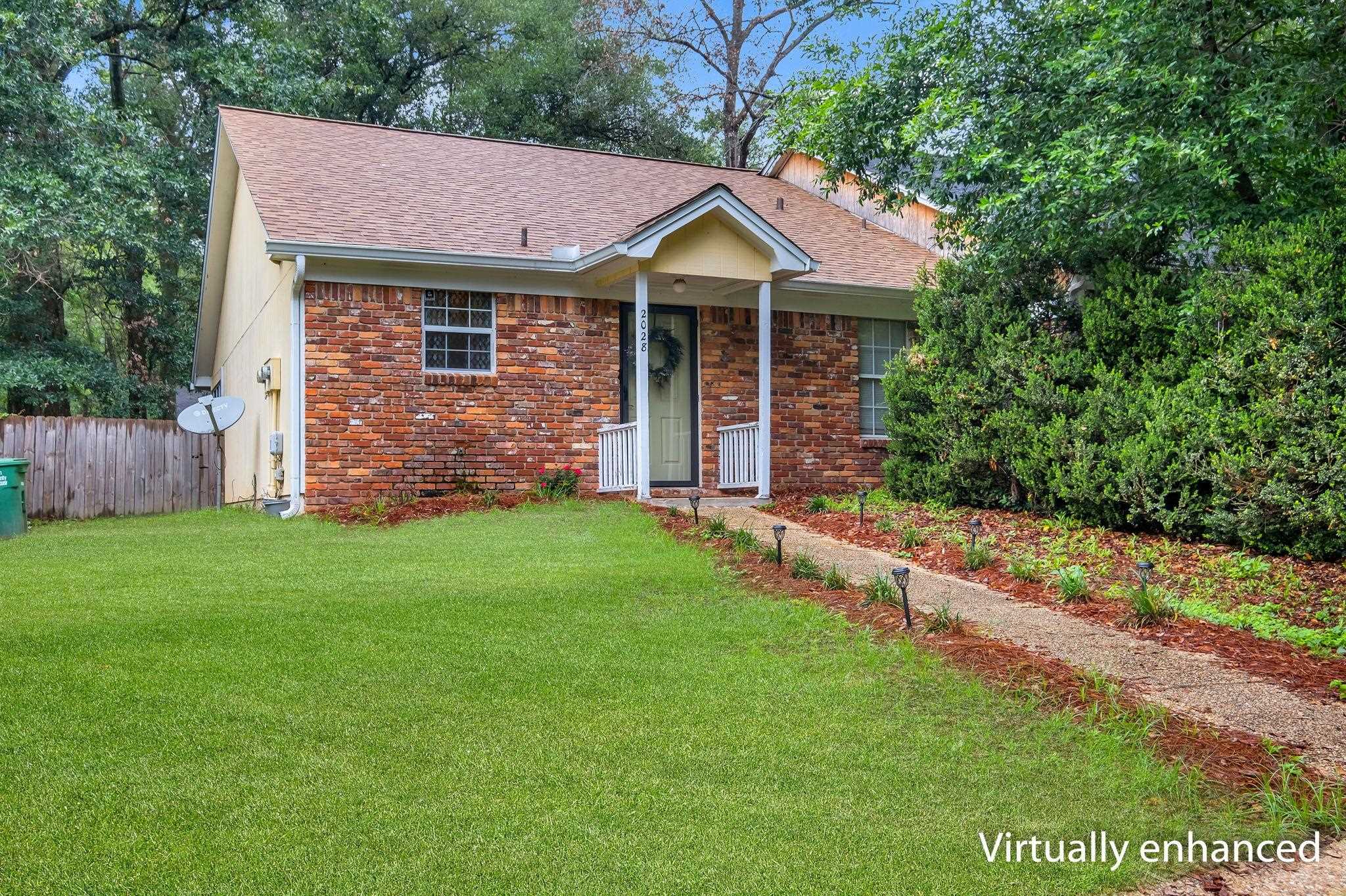 Single-story brick house with a covered porch, landscaped walkway, and broad green lawn.