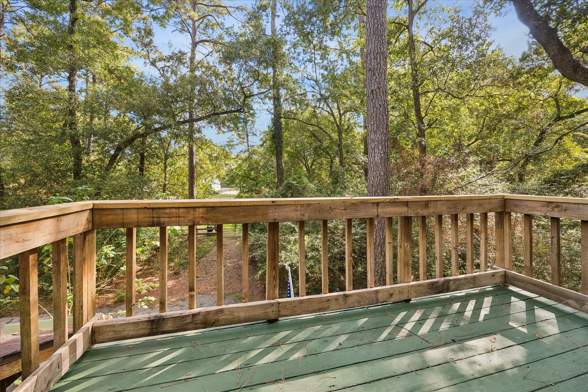 Wooden deck with green-painted floor overlooks a leafy, wooded yard.