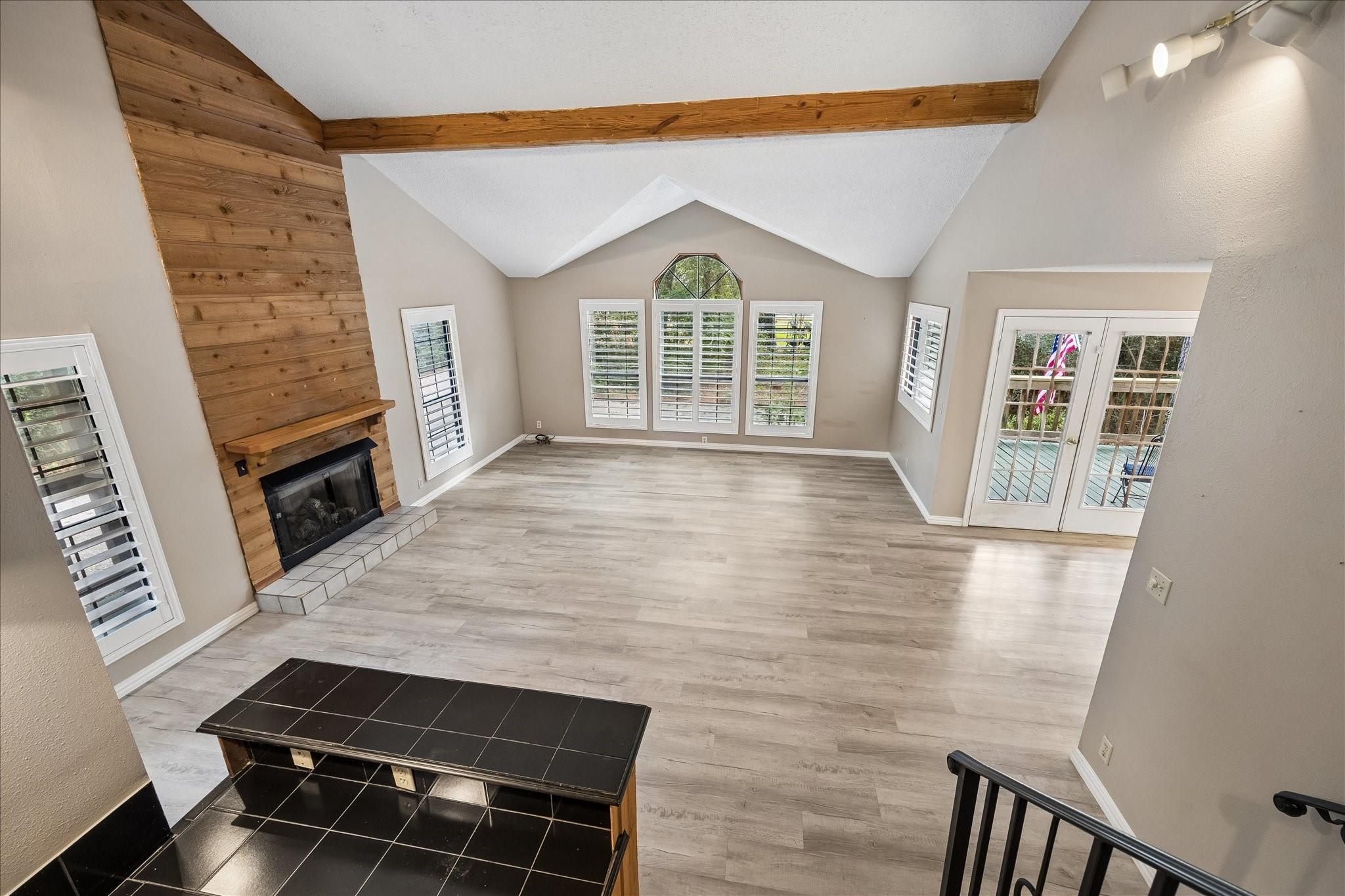 Empty living room with a vaulted ceiling, wood-paneled fireplace, and glass French doors.