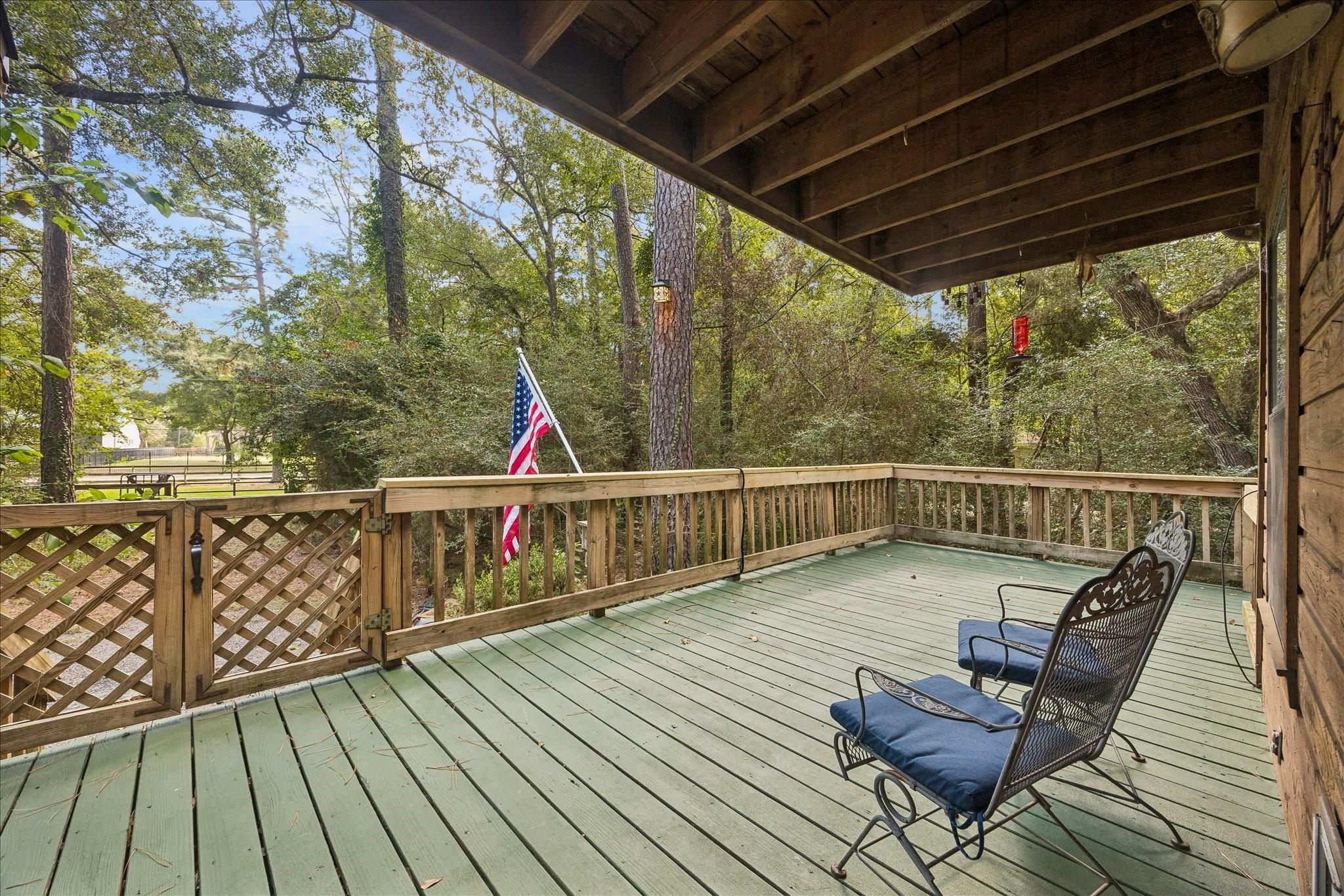 Covered wooden deck with two blue-cushioned chairs overlooking leafy trees.