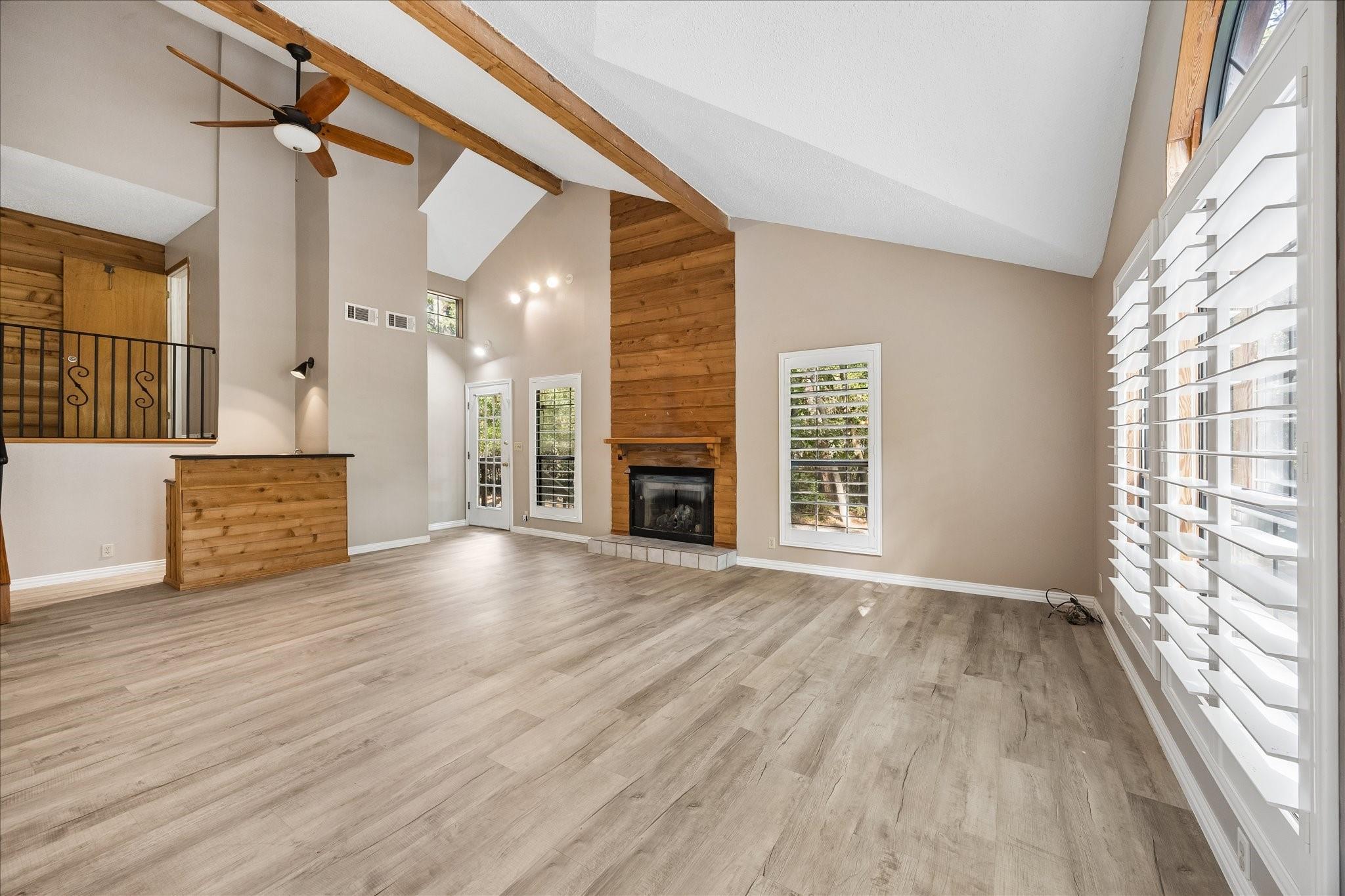 Vacant living room with vaulted wood-beamed ceiling, wood-paneled fireplace, and plantation shutters.