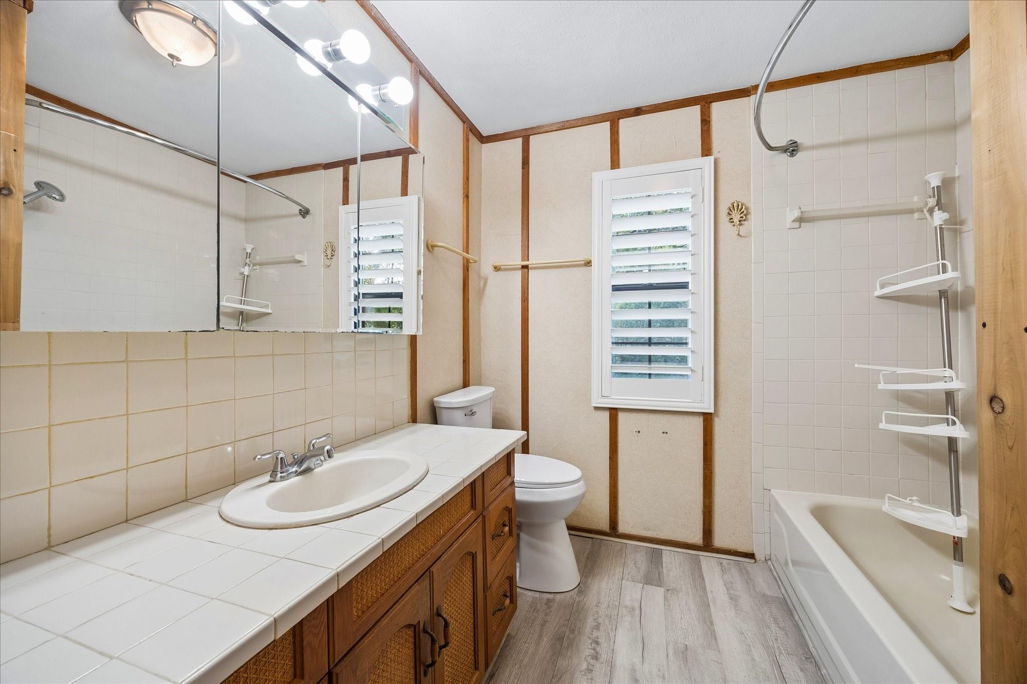 Bathroom with a tiled vanity, wood cabinetry, and a bathtub beneath a tiled shower surround.