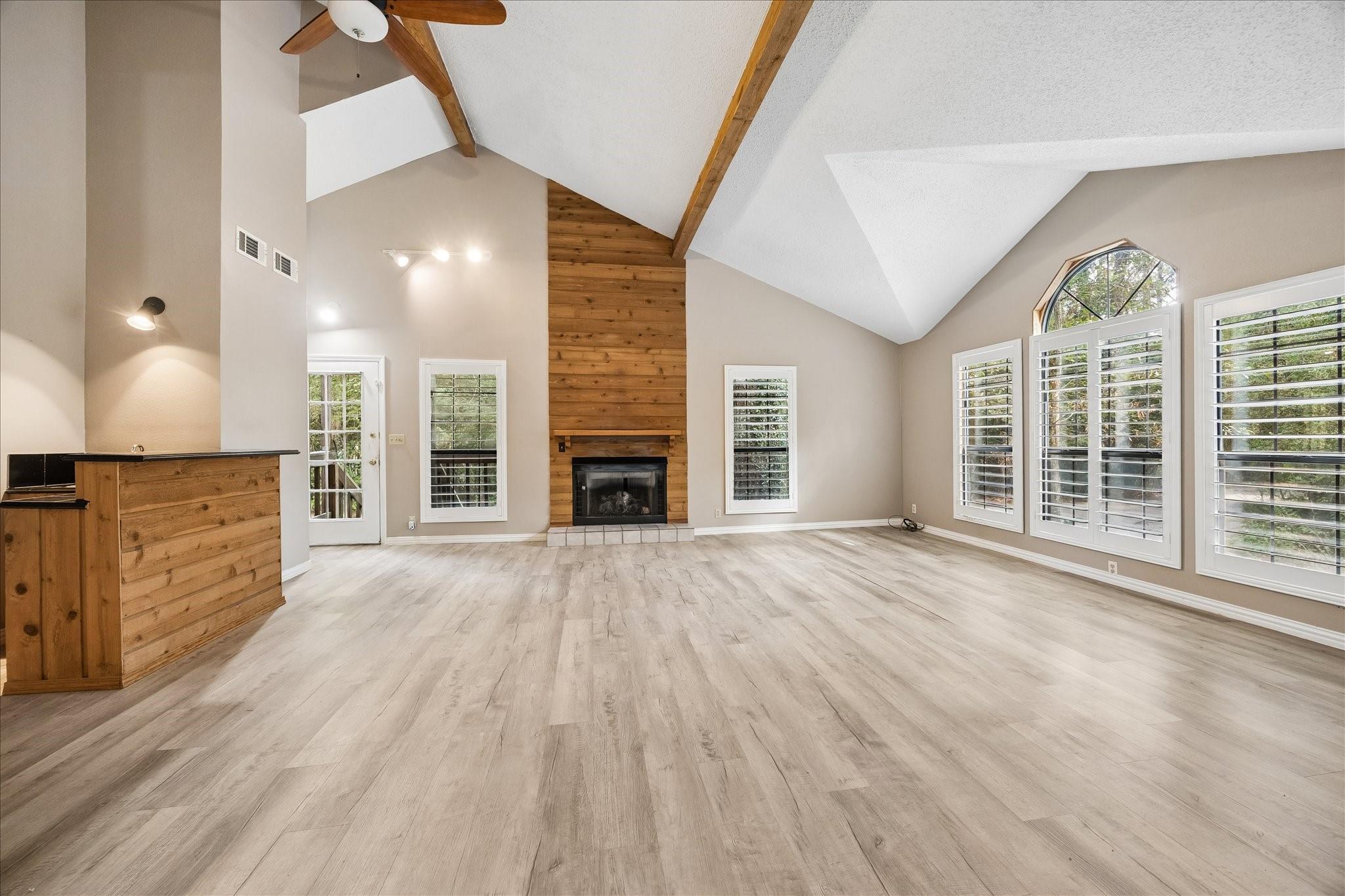 Vacant living room with vaulted ceilings, exposed wood beams, and a tall wood-paneled fireplace.