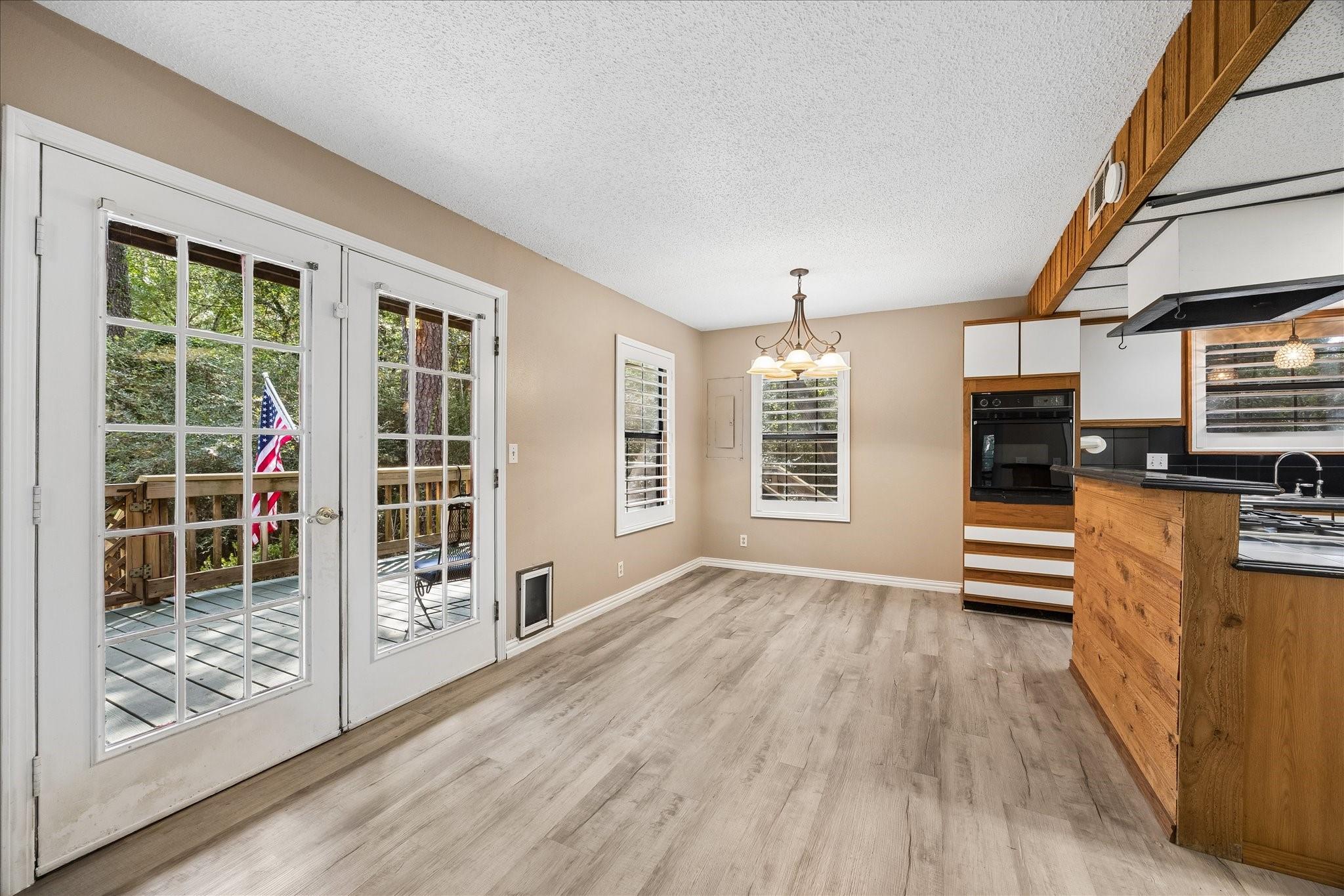 Empty dining area with French doors to a deck and adjoining kitchen with warm wood cabinetry.