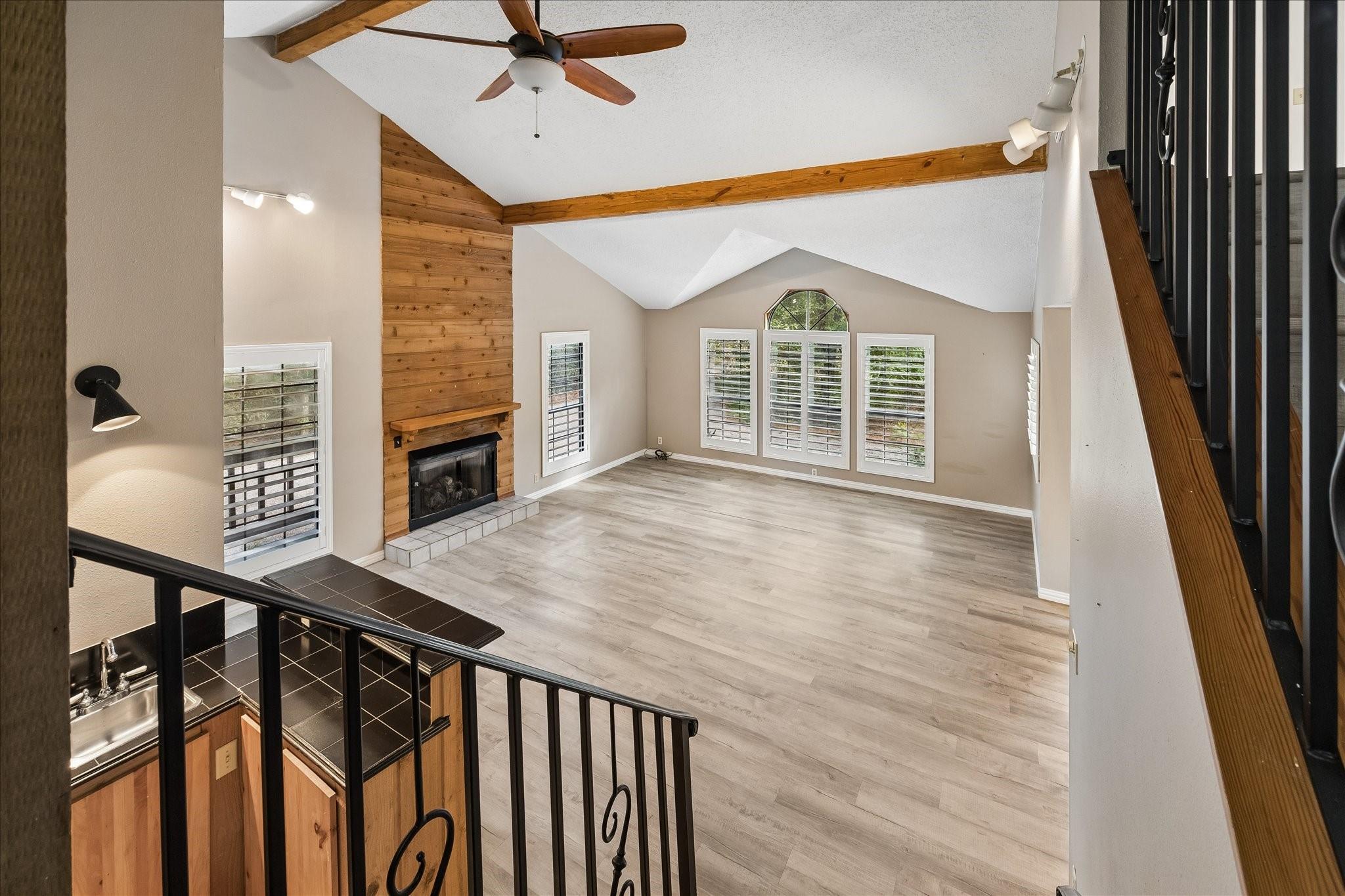 Empty living room with vaulted ceiling, wood-paneled fireplace wall, and shuttered windows.